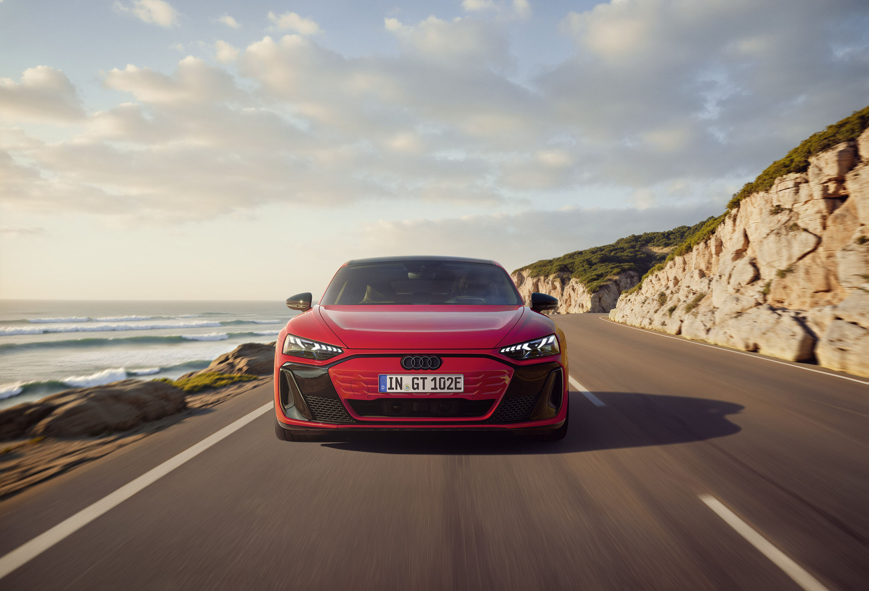 Entering the premium class: Audi e-tron GT quattro combines emotional design, performance, and comfort - At the front of the Audi e-tron GT quattro, a black mask accentuates the inverted Singleframe in the body color. The background shown is AI-generated.