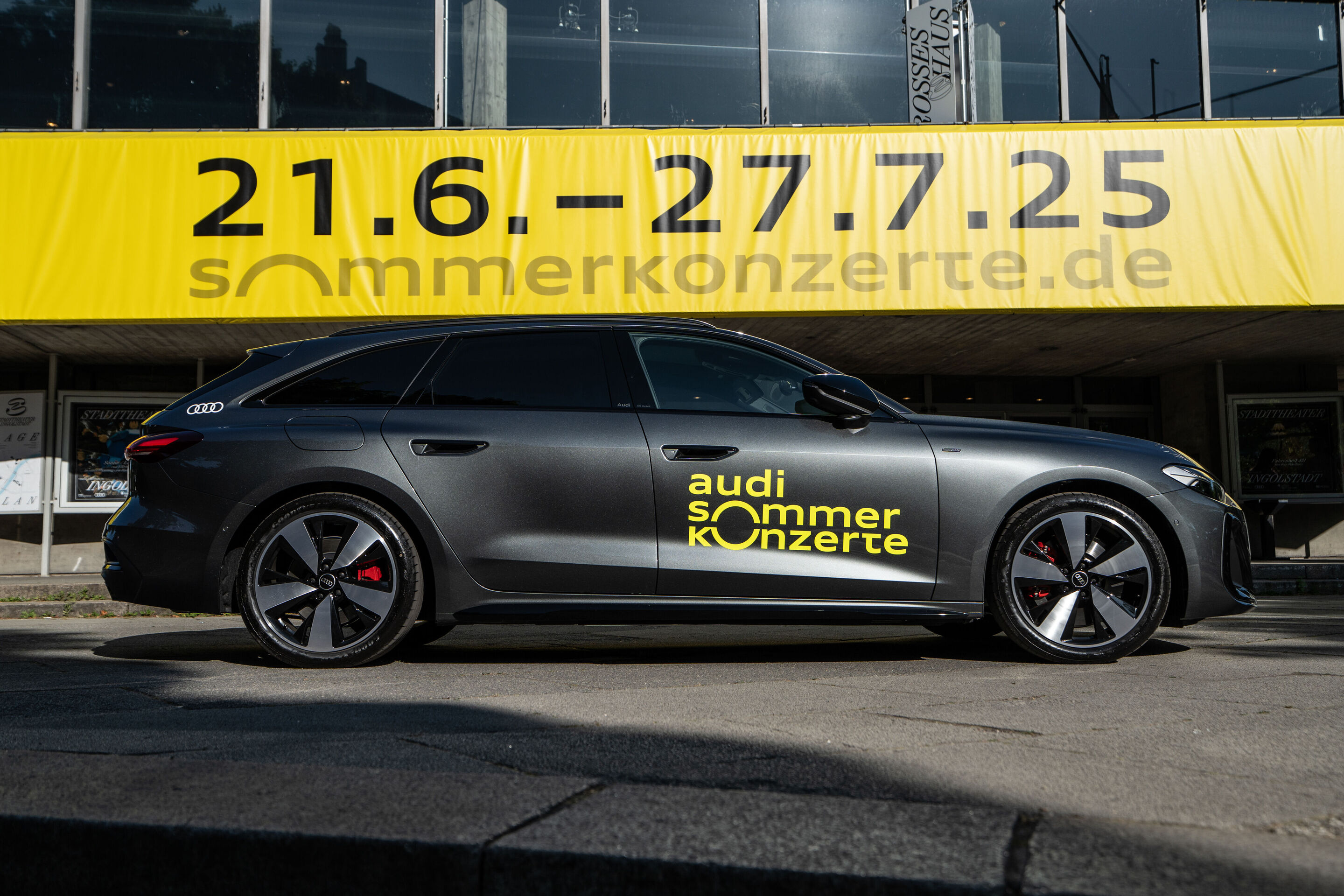 Eröffnungskonzert mit dem Deutschen Symphonie-Orchester Berlin - Ein grauer Audi mit dem gelben Logo der Audi Sommerkonzerte steht vor dem Stadttheater Ingolstadt. Auf einem großen gelben Plakat, das über dem Fahrzeug am Gebäude angebracht ist, steht...