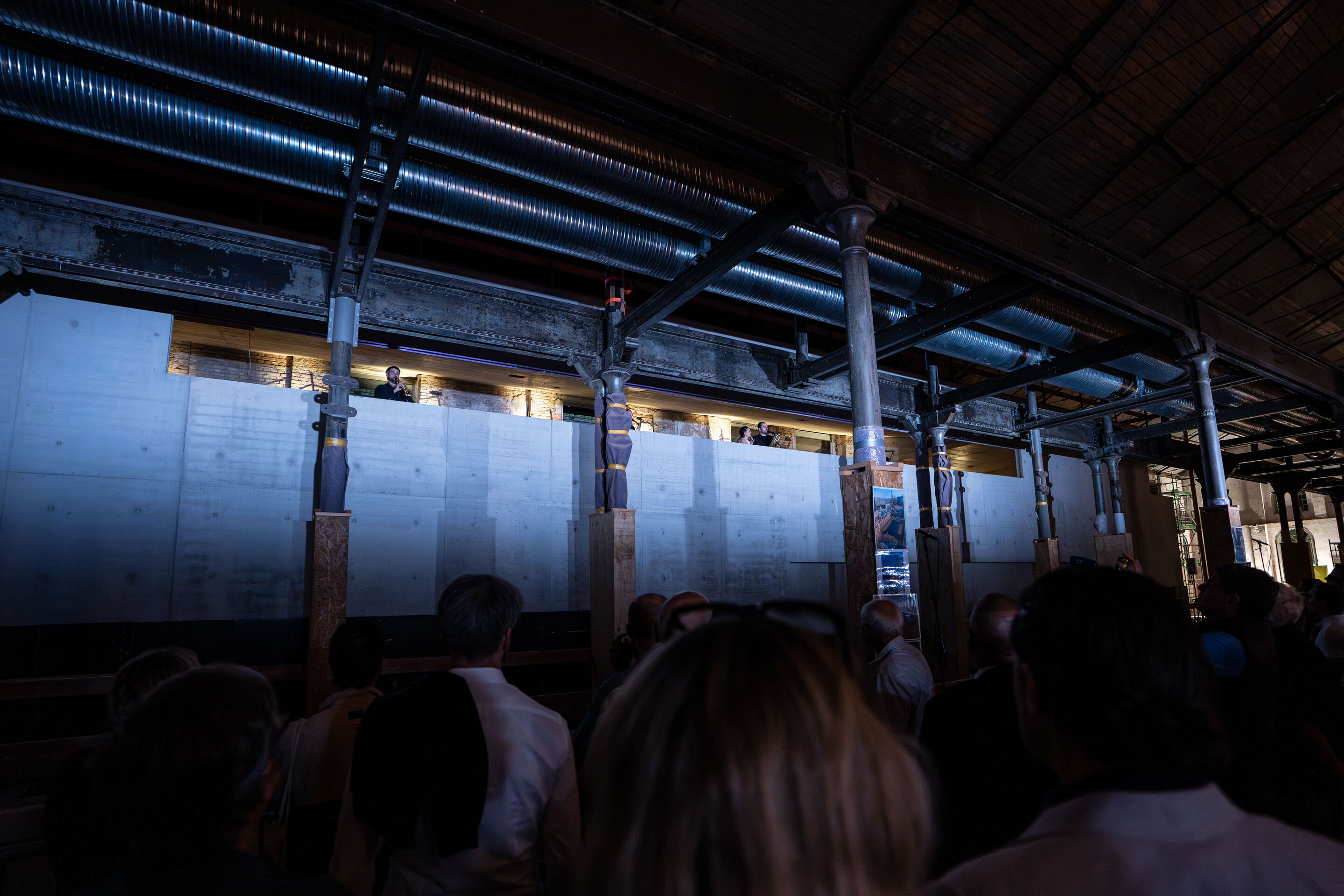“Lux!”: Theatrical concert at the construction site of the MCAD; Arcis Saxophone Quartet, vocal ensemble LauschWerk - On the construction site of the new Museum of Concrete Art and Design Ingolstadt, the audience stands in front of a gray concrete wall...