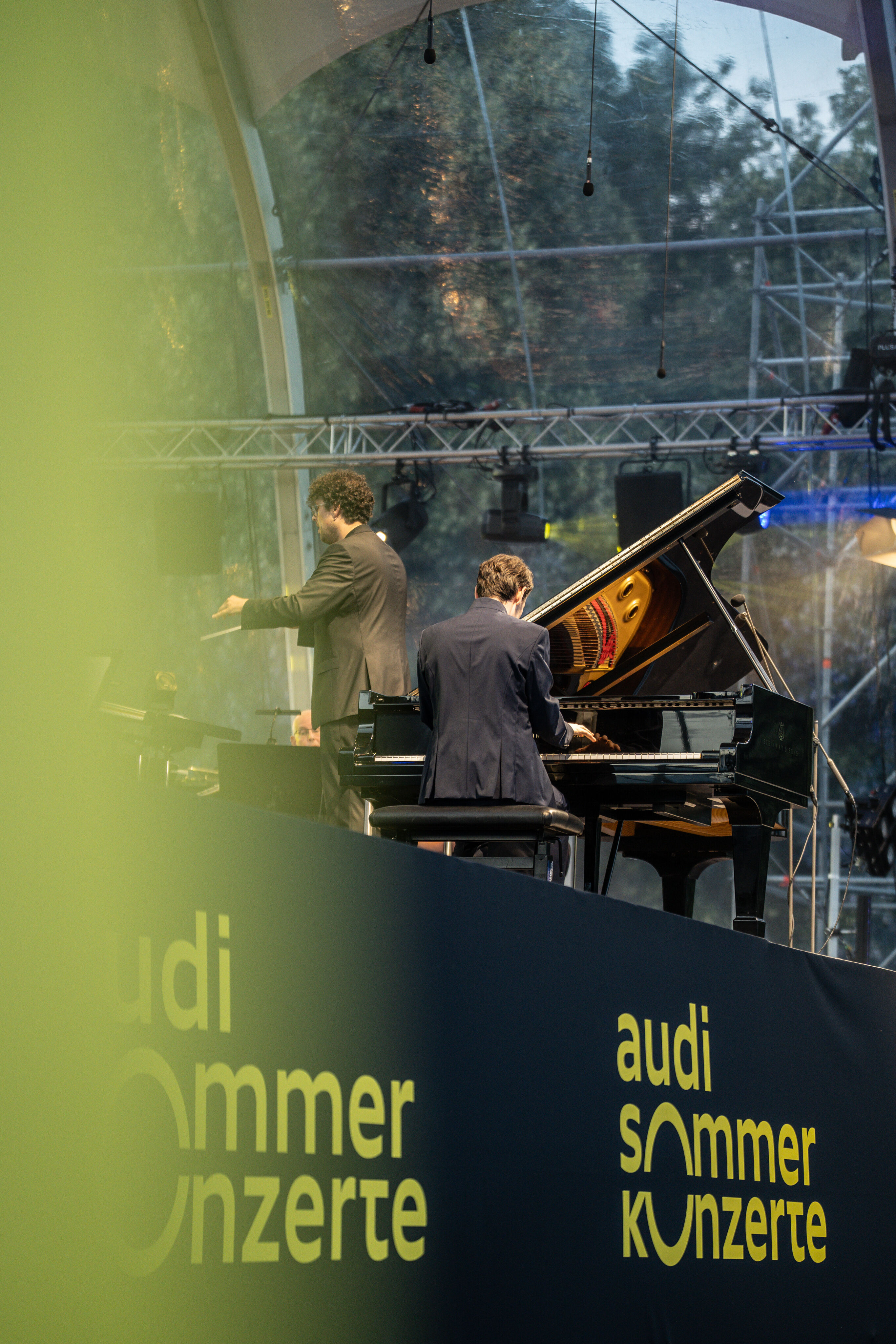 Klassik Open Air – Musical-Highlights mit der Audi Bläserphilharmonie - Beim Klassik Open Air im Klenzepark im Rahmen der Audi Sommerkonzerte ist Florian Glemser zu sehen, wie er auf dem Piano spielt; links neben ihm dirigiert Pietro Sarno, Dirigent der...