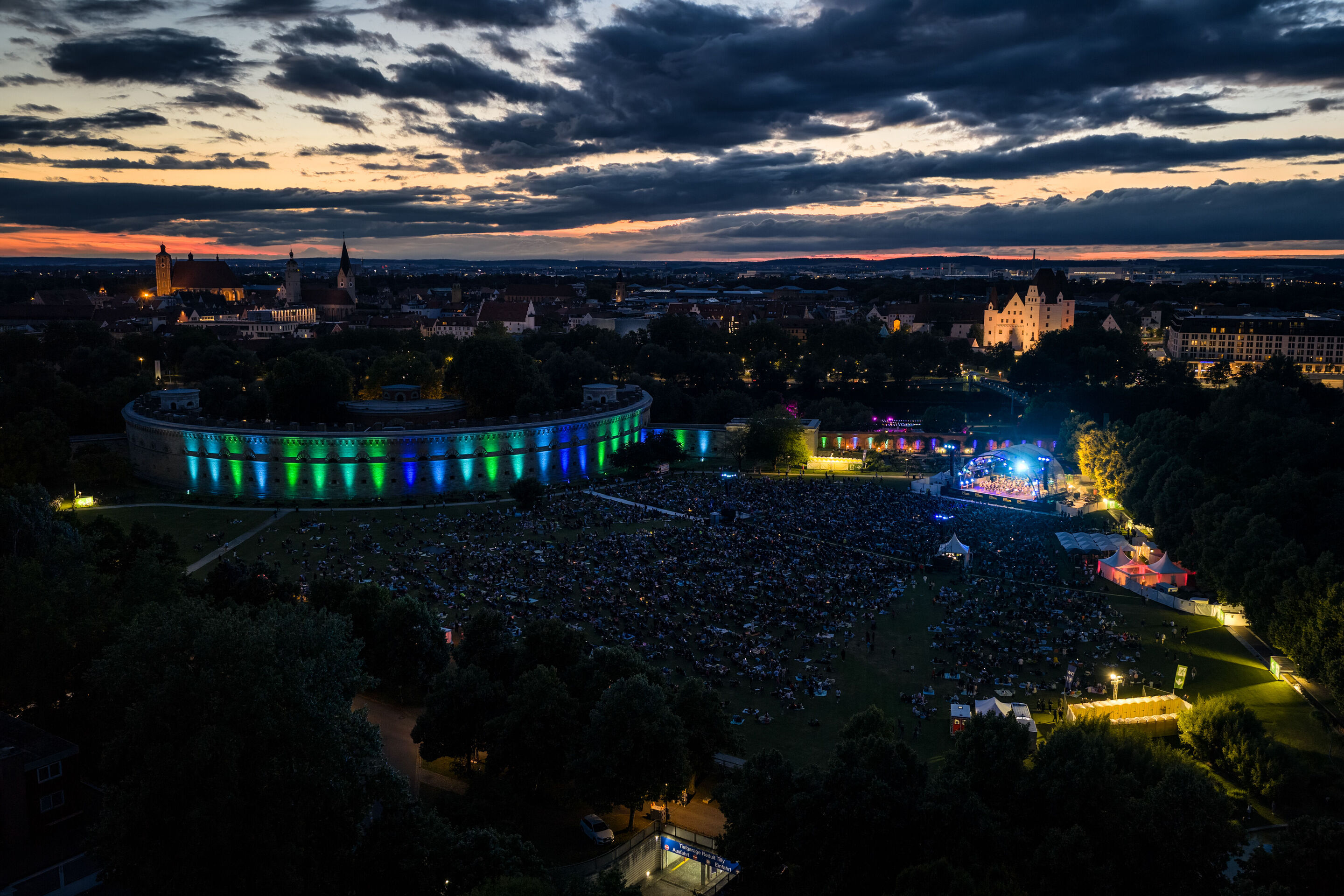 Klassik Open Air – Musical-Highlights mit der Audi Bläserphilharmonie - Blick aus der Vogelperspektive in der Abenddämmerung auf das Klassik Open Air mit der Audi Bläserphilharmonie im Rahmen der Audi Sommerkonzerte im Klenzepark in Ingolstadt; auf der...