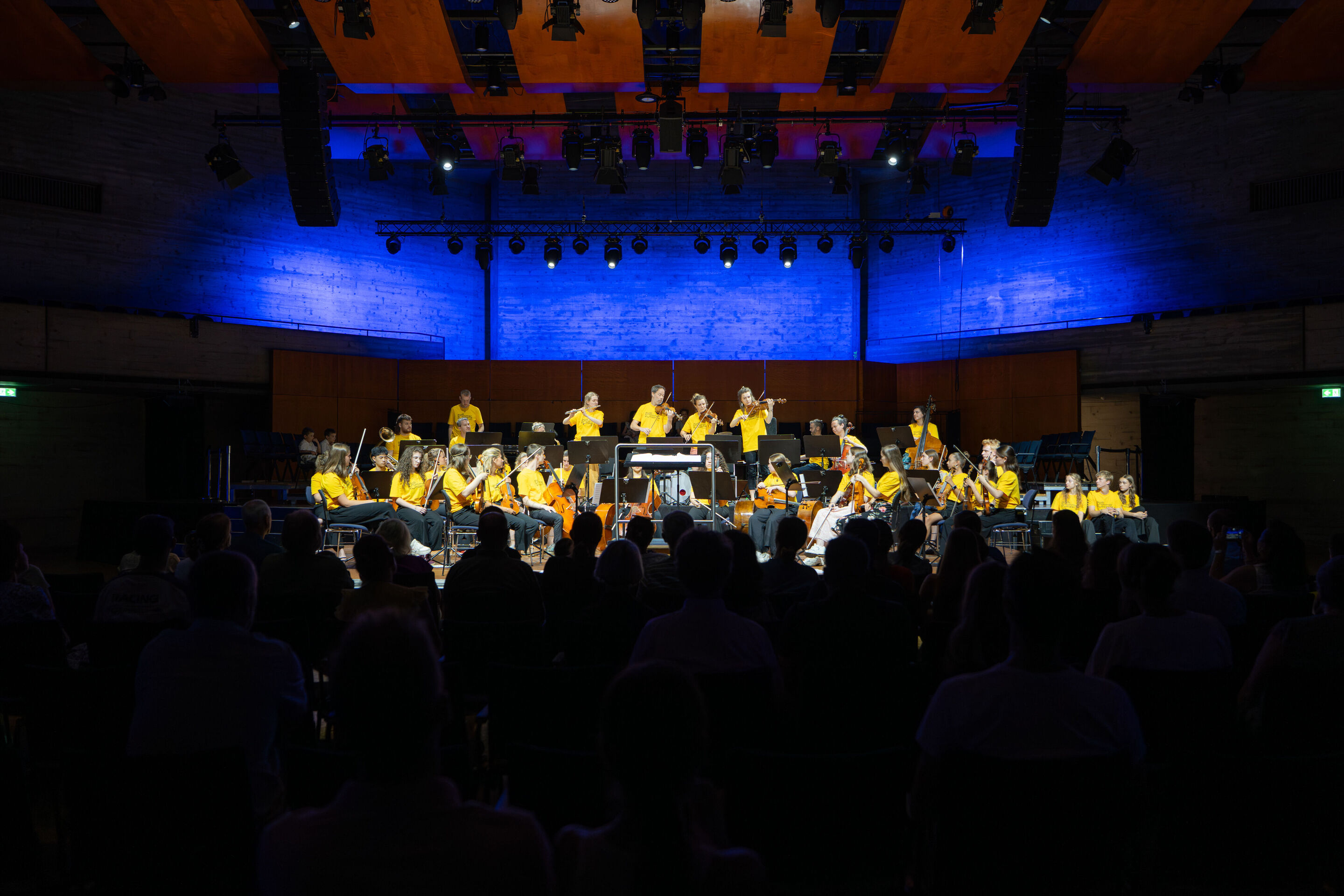 Öffentlicher Workshop mit Schülerinnen und Schülern der Region und dem Aurora Orchestra - Aus Sicht des Publikums musizieren Mitglieder des Aurora Orchestra stehend. Davor sitzen die Schülerinnen und Schüler mit ihren Instrumenten und schauen zu.