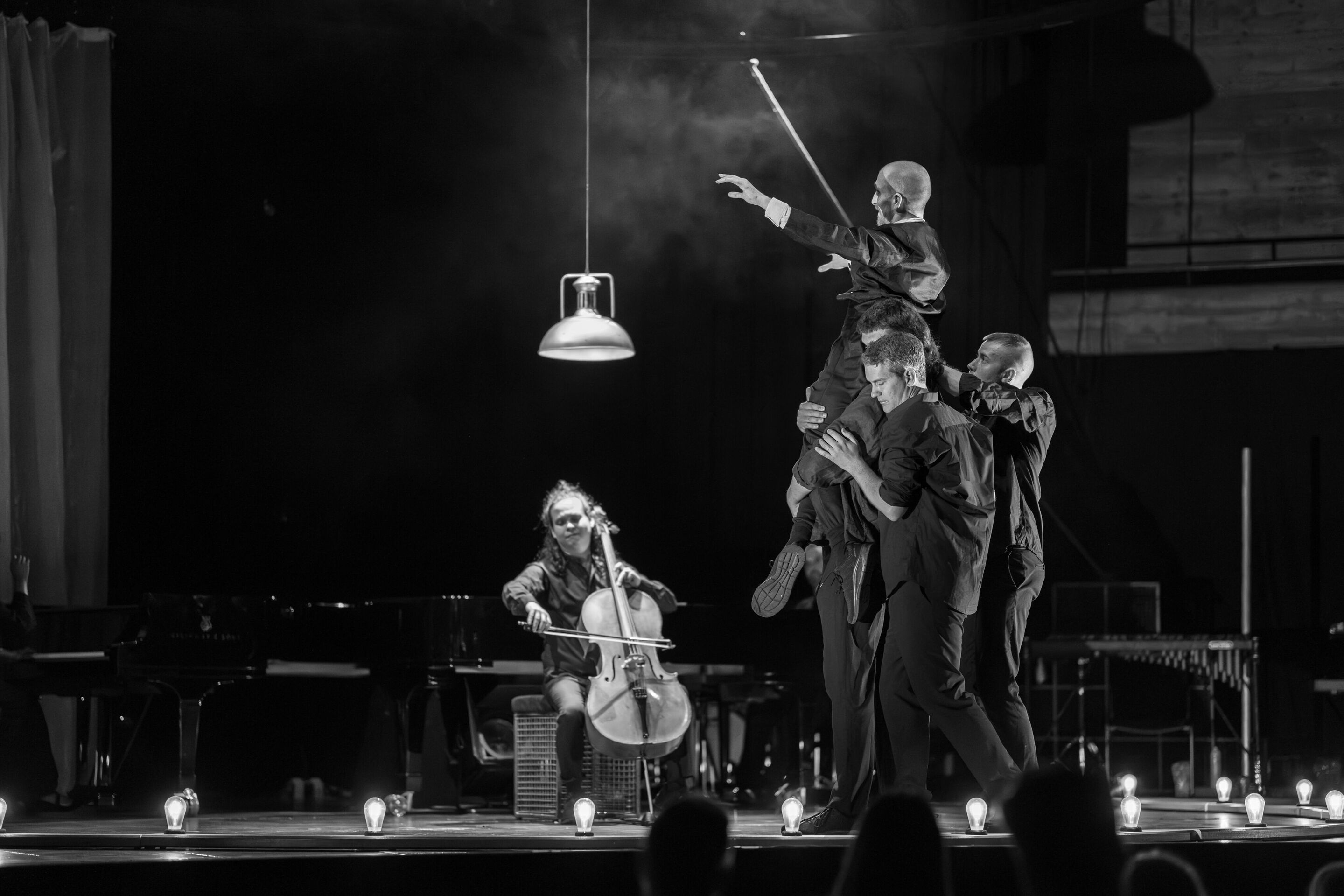 “Carnival”: Theatrical concert for families about the fabulous world of instruments - On the stage of the Festival Hall Ingolstadt, a member of the Aurora Orchestra plays the cello. In front of him, several male members of the Aurora Orchestra lift dancer...