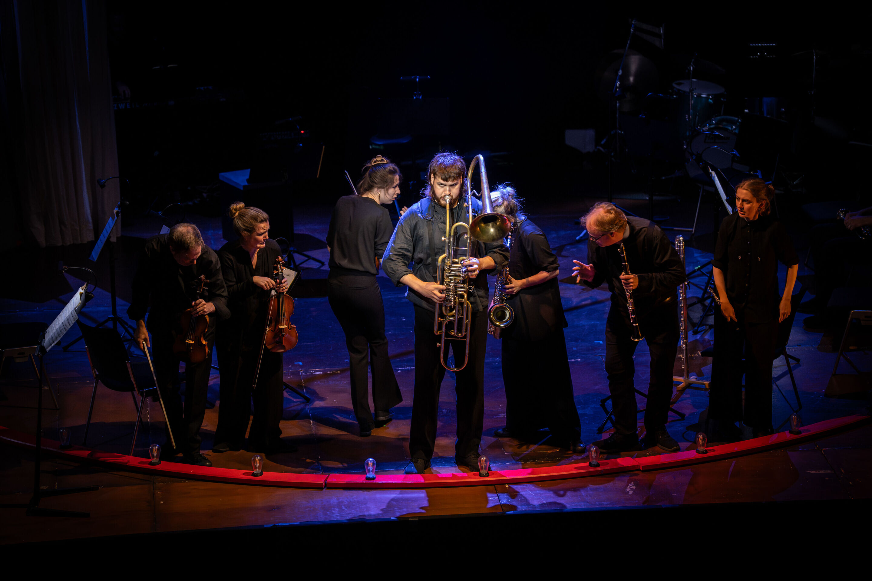 “Carnival”: Theatrical concert for families about the fabulous world of instruments - On the stage of the Festival Hall Ingolstadt, a member of the Aurora Orchestra plays a cimbasso. Behind him, other members of the orchestra can be seen.