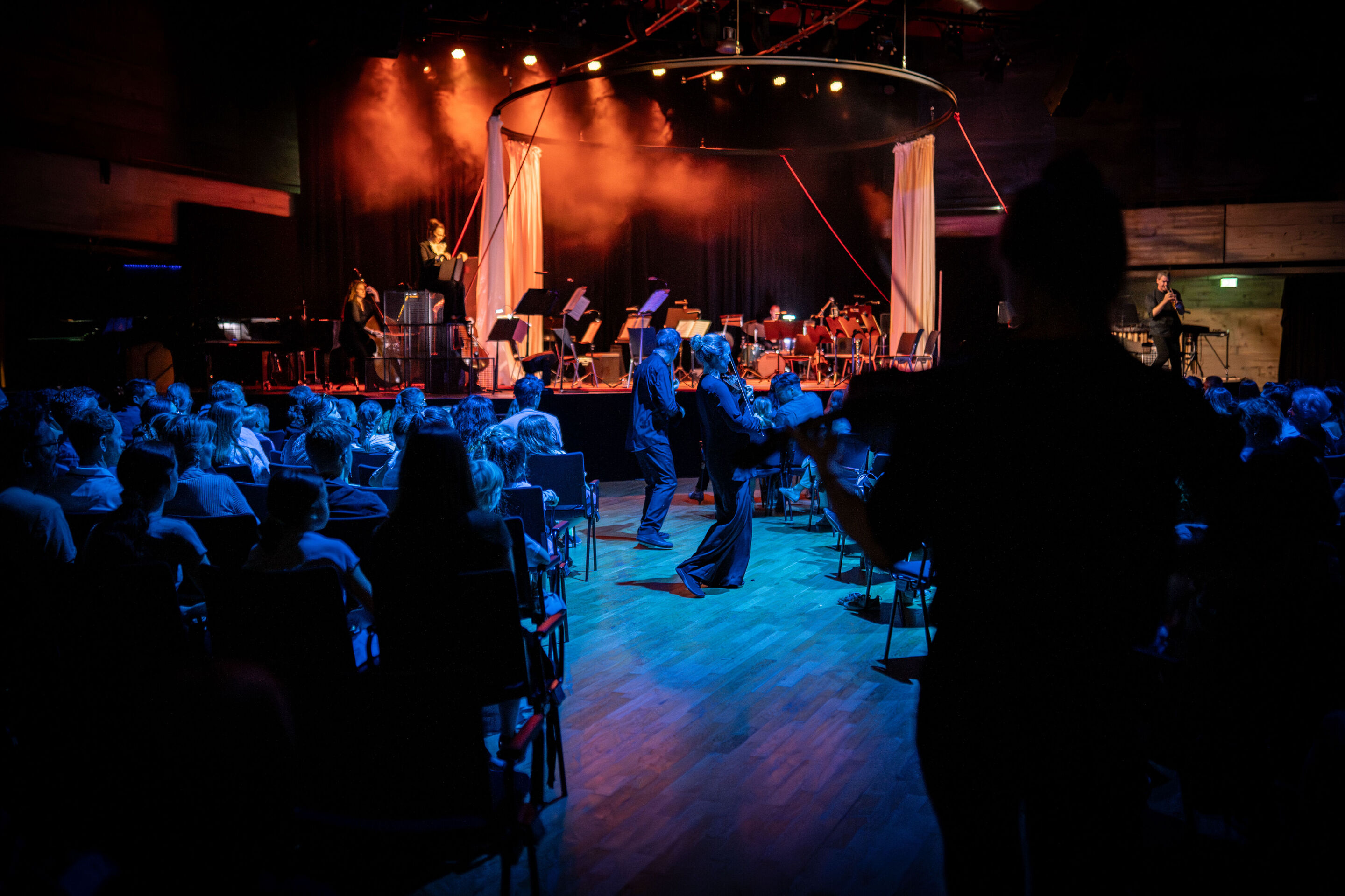 “Carnival”: Theatrical concert for families about the fabulous world of instruments - In the Festival Hall Ingolstadt, several members of the Aurora Orchestra perform standing among the audience. In the background on stage, narrator Birgit Minichmayr...