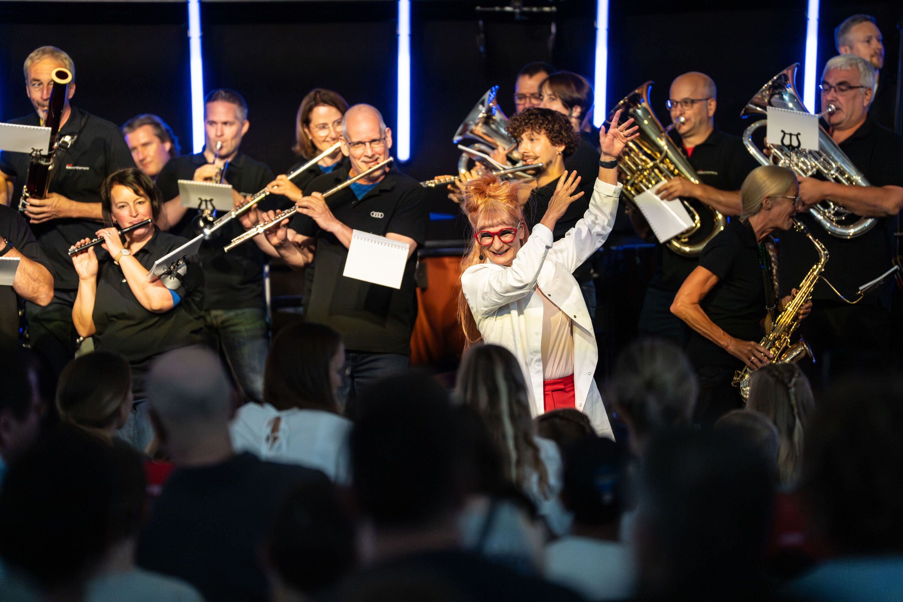“ADUI und die Kraft der magischen Ringe”: children’s concert with the Audi Philharmonic Wind Orchestra - From the audience's perspective in H6, scientist Olivia Wendt is seen in the center, behind are the musicians of the Audi Philharmonic Wind Orchestra...