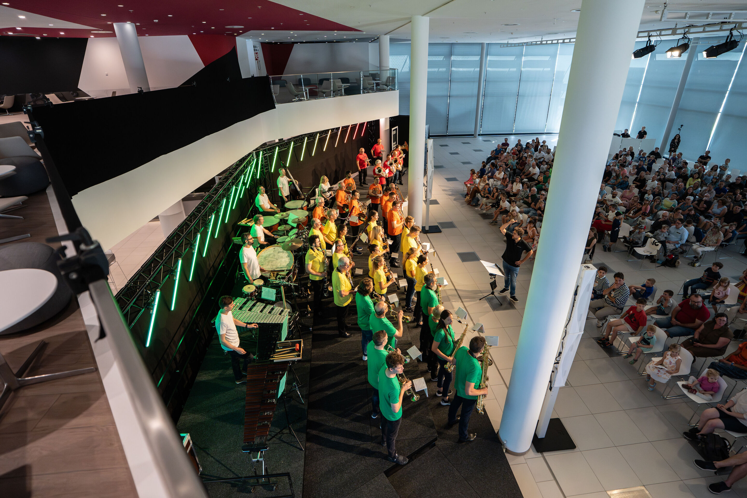 “ADUI und die Kraft der magischen Ringe”: children’s concert with the Audi Philharmonic Wind Orchestra - From above, the stage in H6 shows the musicians of the Audi Philharmonic Wind Orchestra with conductor Pietro Sarno and the audience.