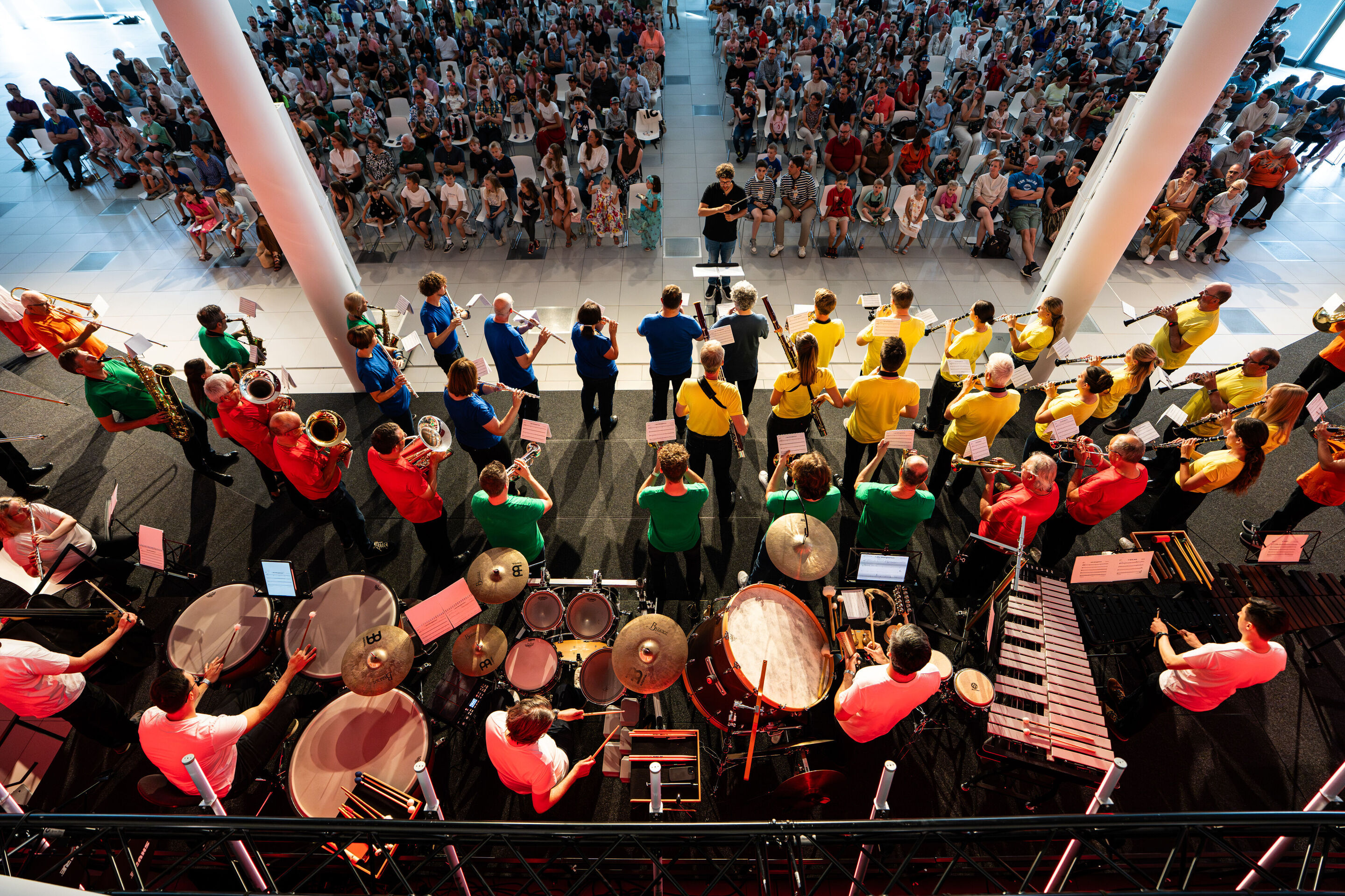 „ADUI und die Kraft der magischen Ringe“: Kinderkonzert mit der Audi Bläserphilharmonie - Beim Kinderkonzert der Audi Sommerkonzerte im H6 spielt die Audi Bläserphilharmonie unter der Leitung von Pietro Sarno. Die Musiker tragen bunte T-Shirts, im Hintergrund...