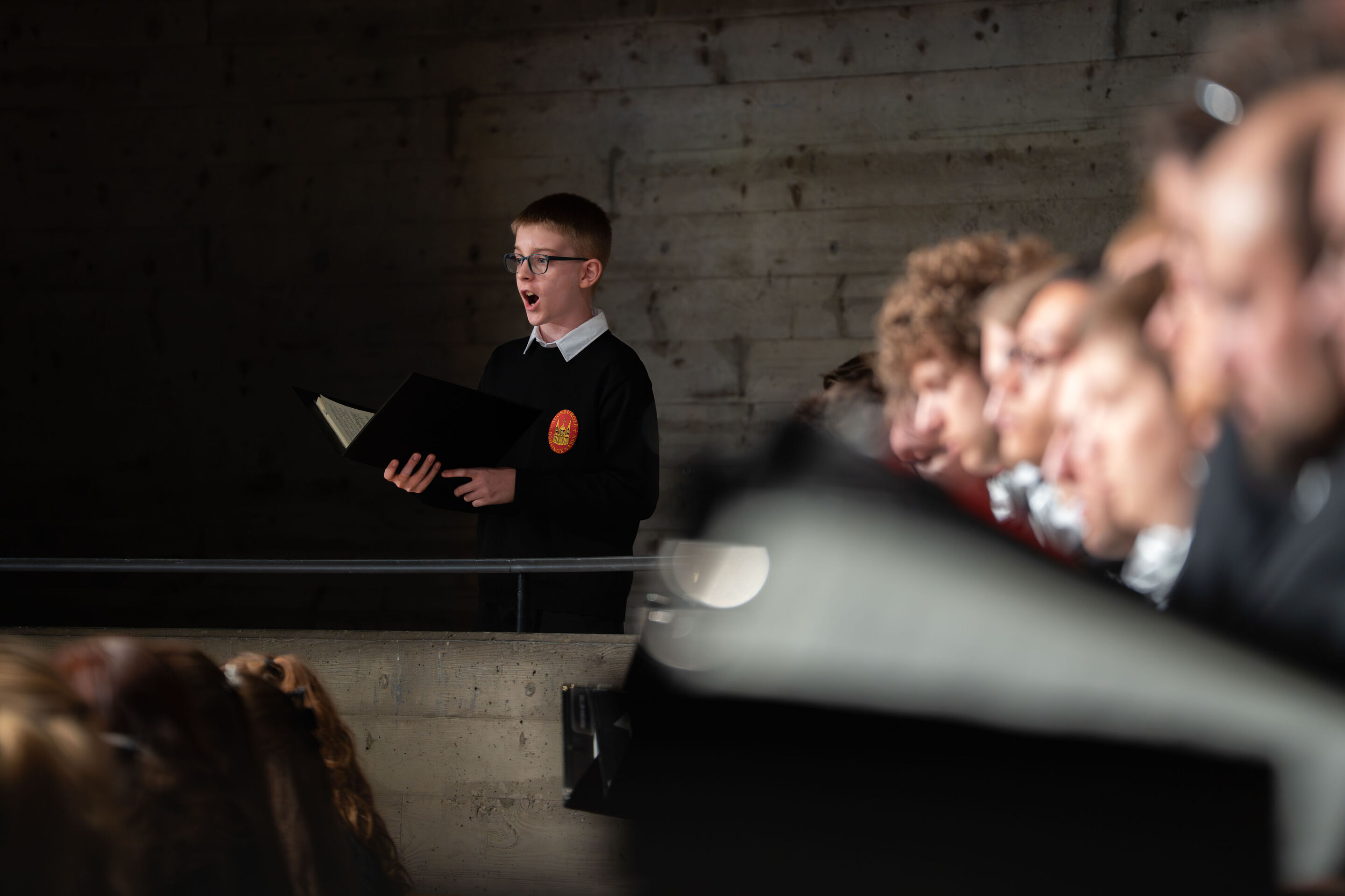 Mendelssohns „Elias“ mit der Audi Jugendchorakademie - Im Rang links des Festsaals Ingolstadt singt Ferdinand Lidl, Knabensolist der Augsburger Domsingknaben, mit einem Notenbuch in den Händen. Rechts im Bild musizieren Mitglieder der Audi Jugendchorakademie.