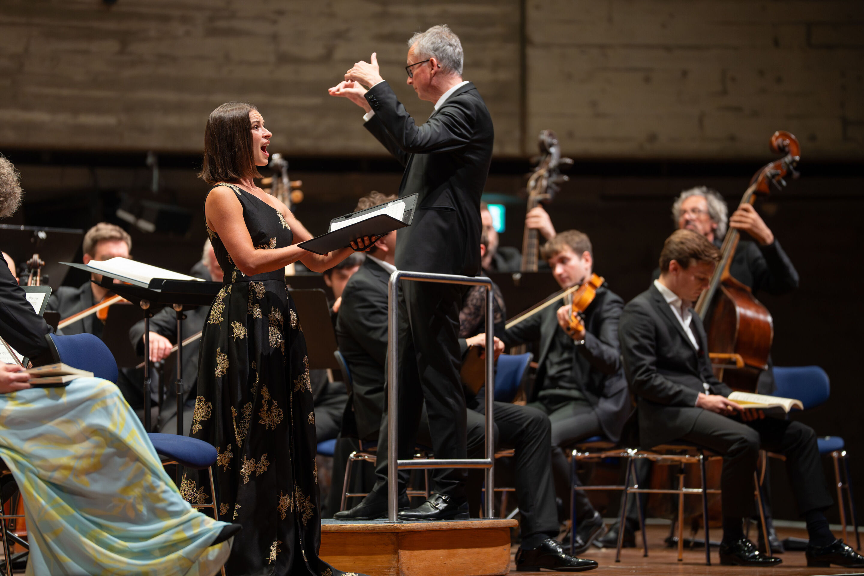 Mendelssohns „Elias“ mit der Audi Jugendchorakademie - Auf der Bühne des Festsaals Ingolstadt singt Sopranistin Marie-Sophie Pollak stehend mit einem Notenbuch in den Händen. Rechts von ihr dirigiert Martin Steidler auf dem Dirigentenpult die Musizierenden...