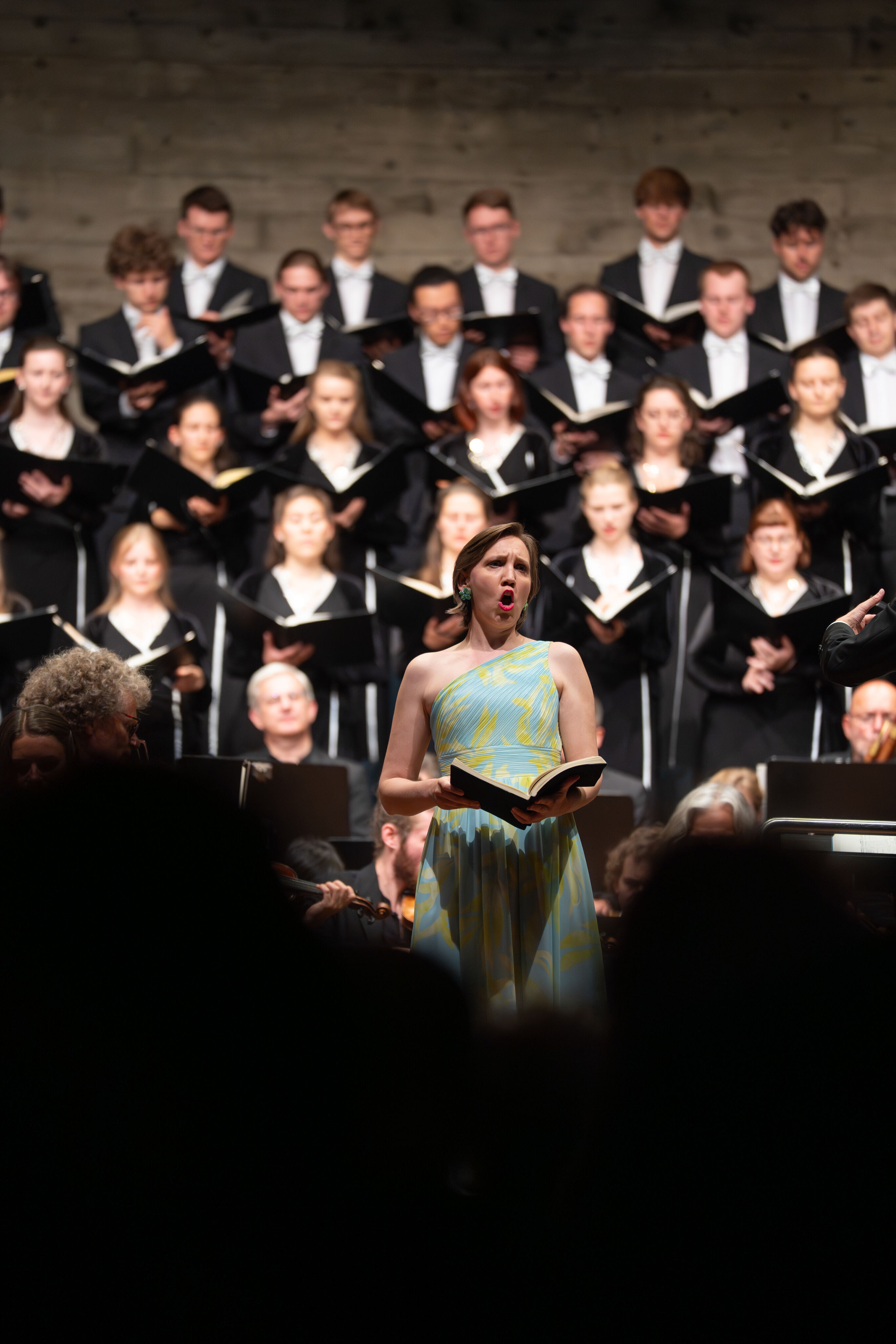 Mendelssohns „Elias“ mit der Audi Jugendchorakademie - Sängerin Ulrike Malotta (Alt) steht singend mit dem Notenbuch in den Händen. Im Hintergrund ist verschwommen die Audi Jugendchorakademie zu sehen.