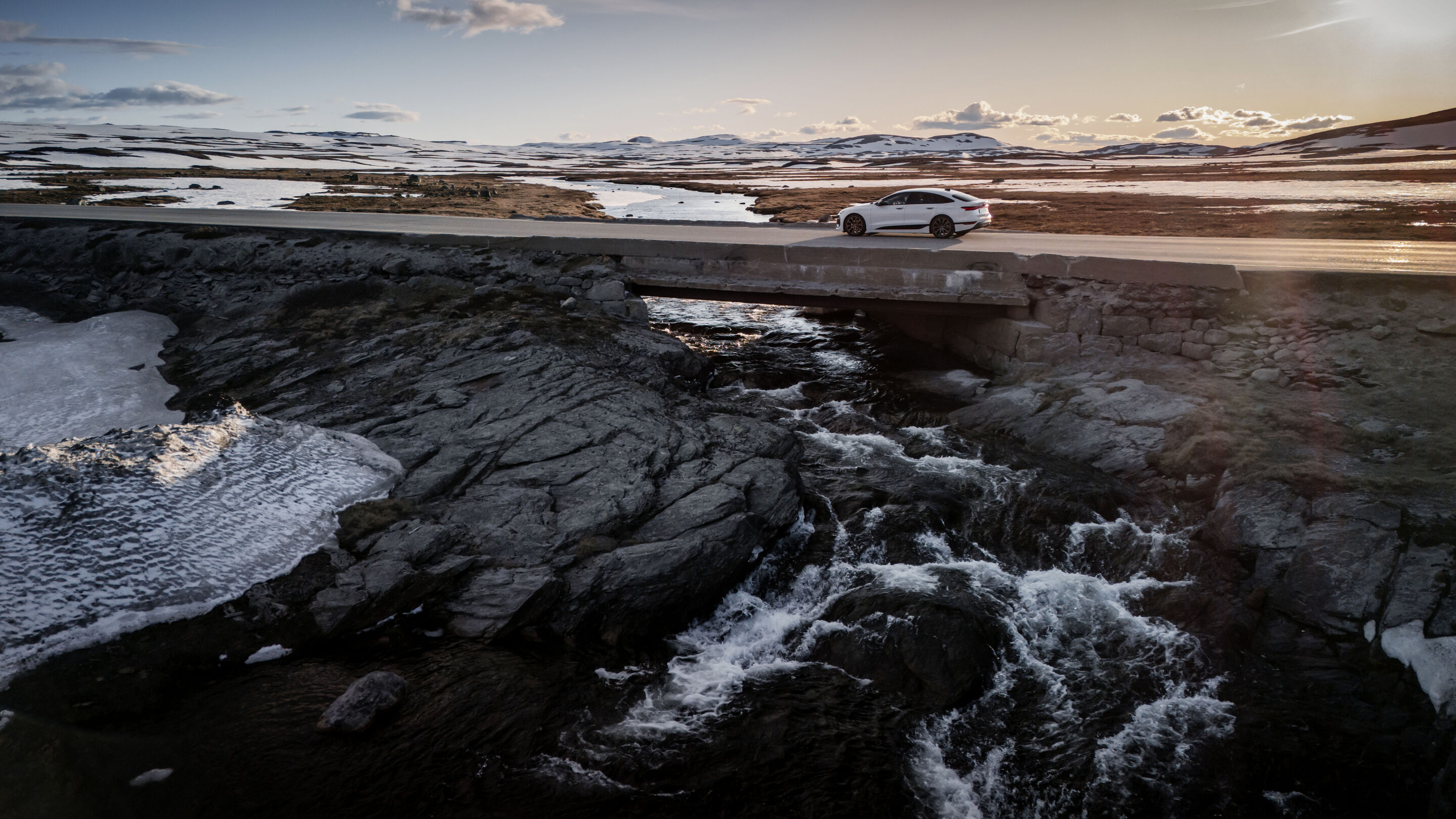 All charged up: from Copenhagen to Bergen in the A6 e-tron - An Audi A6 Sportback e-tron in Glacier white metallic crosses a short bridge over a rushing river. The vast Norwegian landscape can be seen in the background.