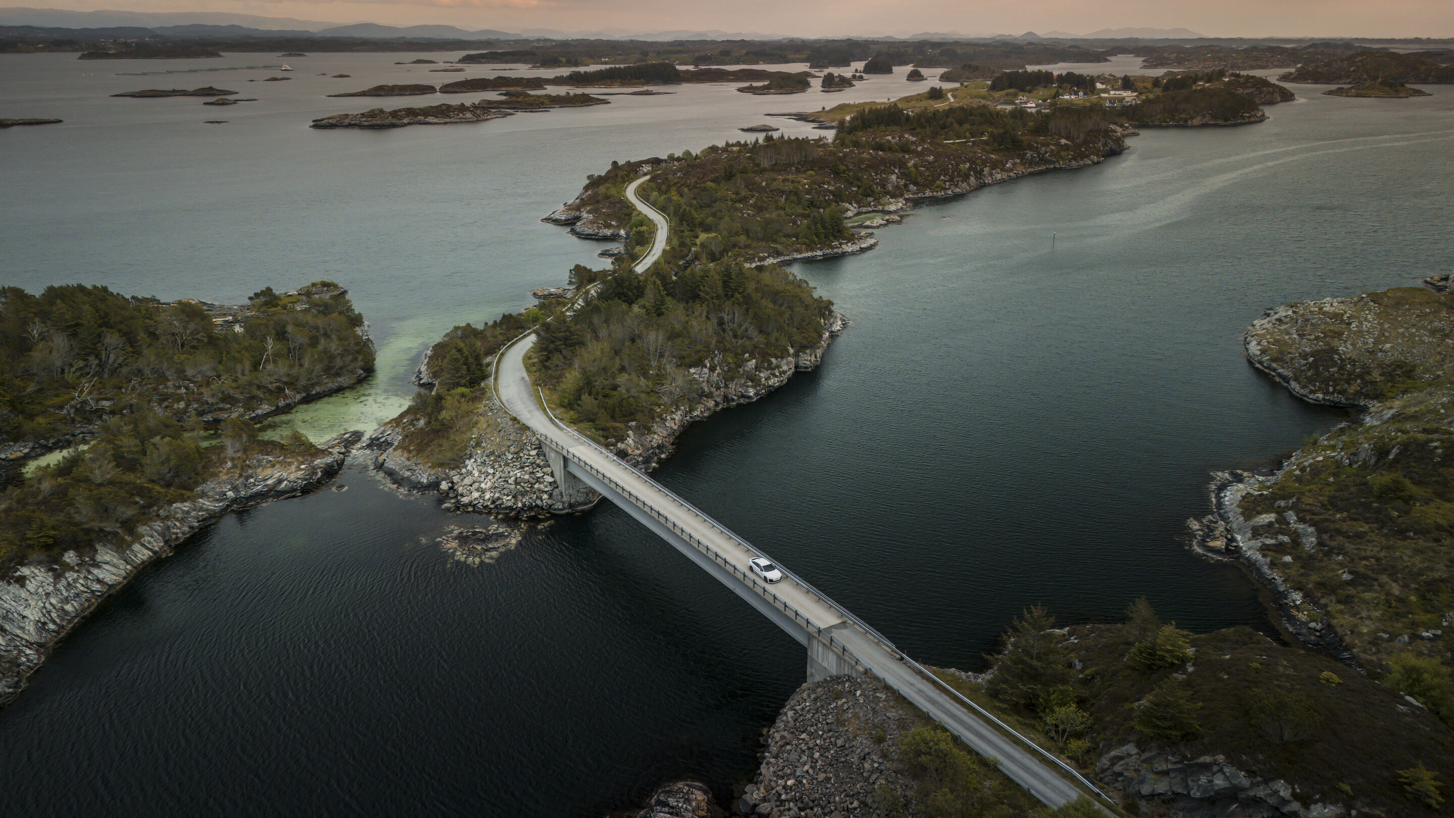 All charged up: from Copenhagen to Bergen in the A6 e-tron - An Audi A6 Sportback e-tron in Glacier white metallic crosses a bridge in Norway’s rugged coastal landscape. There are numerous small islands in the background.