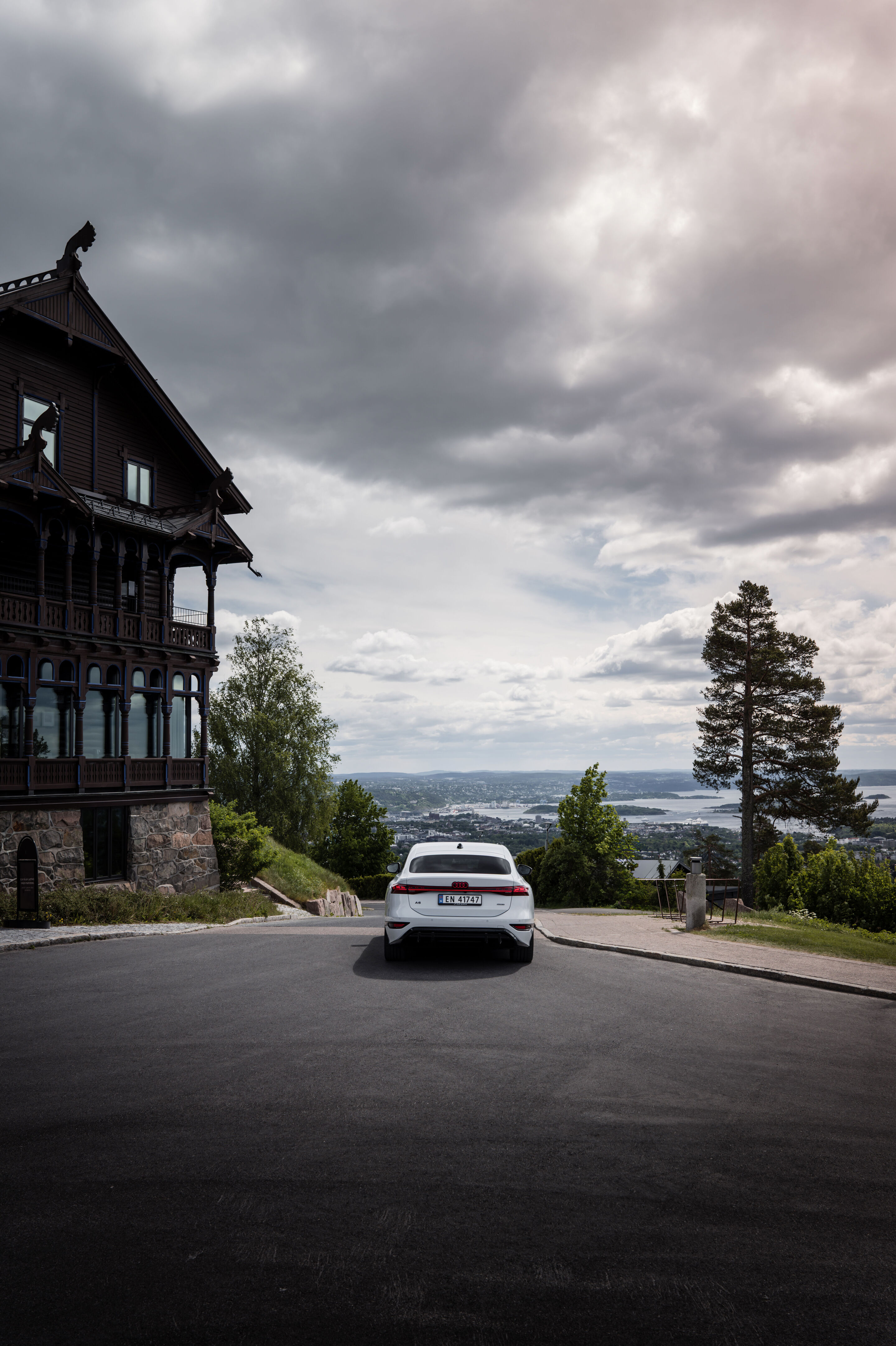 All charged up: from Copenhagen to Bergen in the A6 e-tron - An Audi A6 Sportback e-tron in Glacier white metallic is parked to the right of a Scandinavian-style hotel, with Oslo visible in the distance.