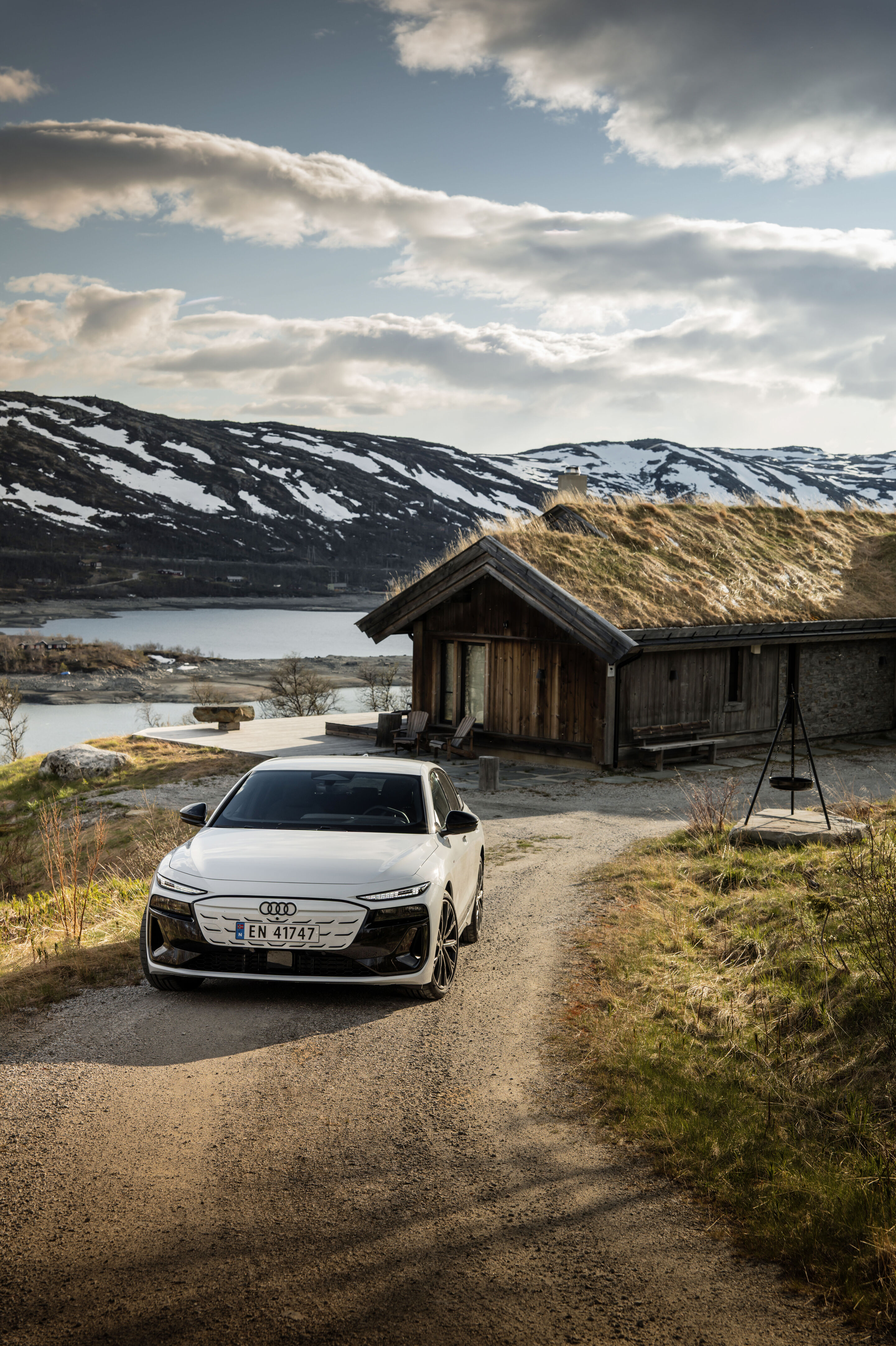 All charged up: from Copenhagen to Bergen in the A6 e-tron - An Audi A6 Sportback e-tron in Glacier white metallic is parked on a gravel road that leads to a house of classic Scandinavian design.