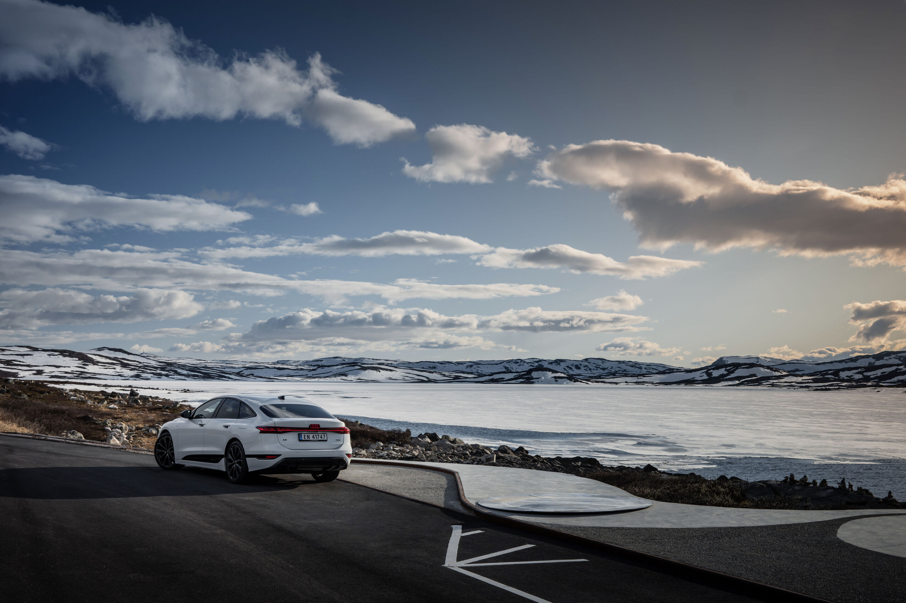 All charged up: from Copenhagen to Bergen in the A6 e-tron - An Audi A6 Sportback e-tron in Glacier white metallic sits in a parking area directly next to an icy body of water in Norway. Snow-covered hills are visible in the distance.