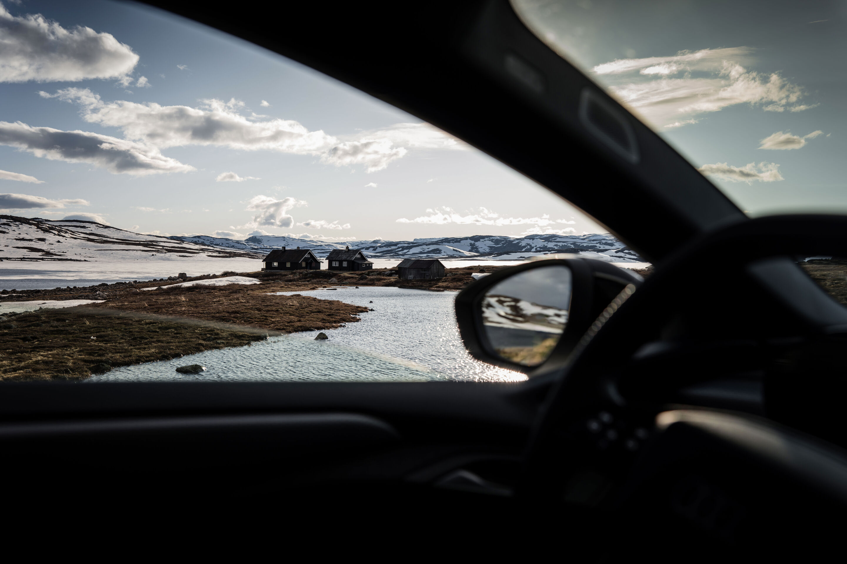 All charged up: from Copenhagen to Bergen in the A6 e-tron - Looking out from the interior of an Audi A6 Sportback e-tron, the view falls on a group of three Norwegian-style houses with water in the foreground. A snow-covered landscape is visible in the...
