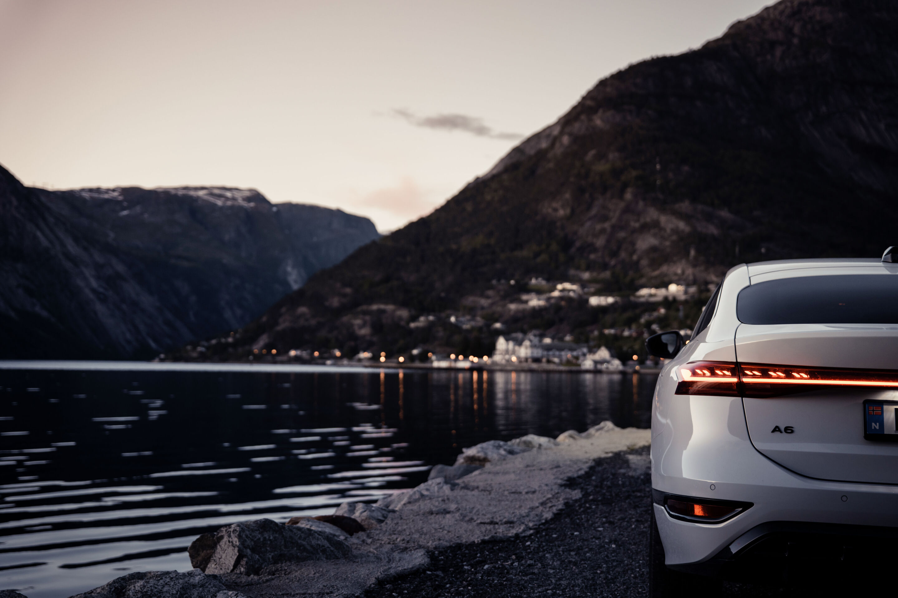 Strom aufwärts: Im Audi A6 e-tron von Kopenhagen nach Bergen - Ein Audi A6 Sportback e-tron in Gletscherweiß Metallic steht auf einem Parkplatz in Norwegen. Im Hintergrund befindet sich vereistes Gewässer mit verschneiten Hügeln.