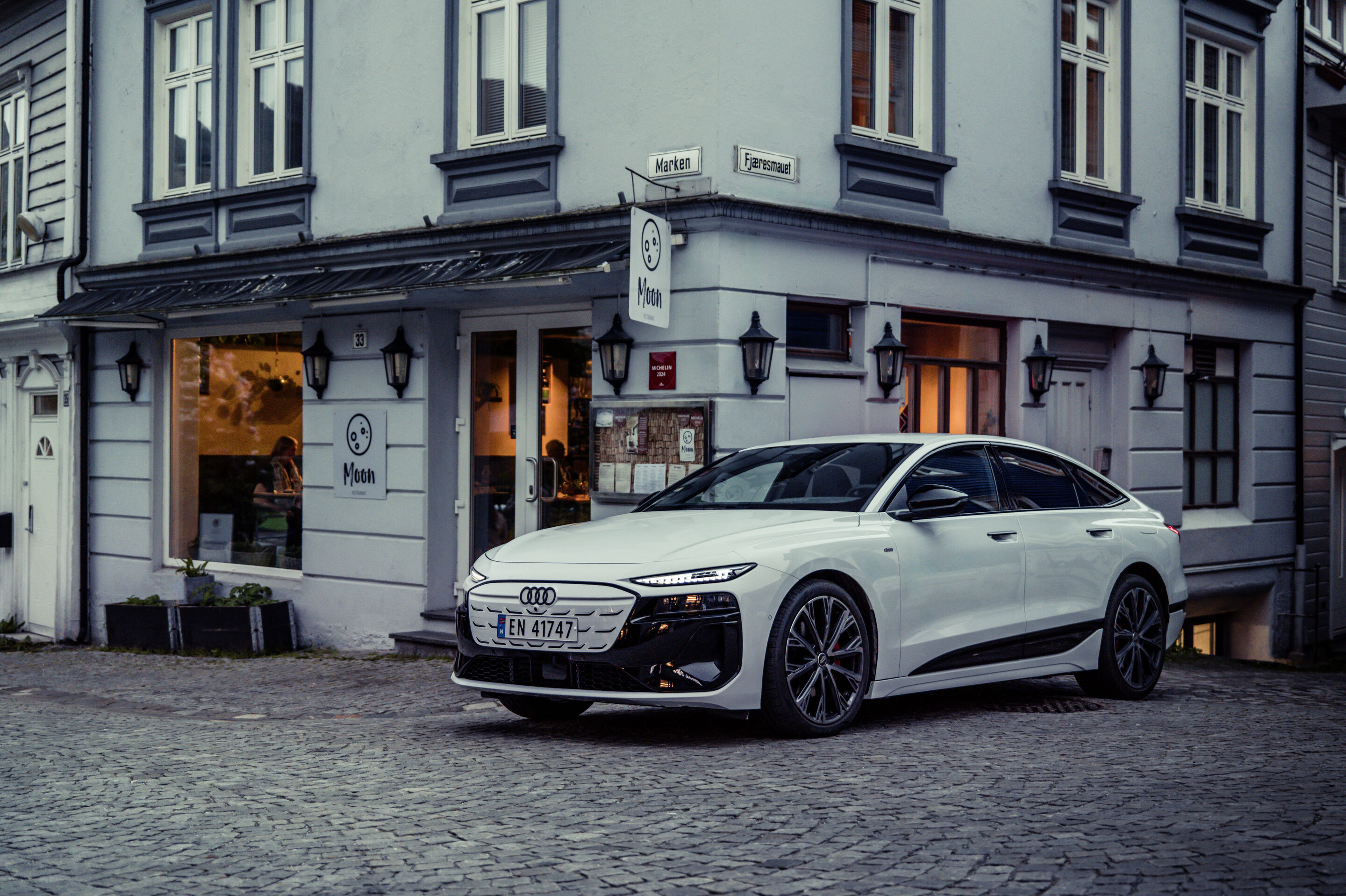 All charged up: from Copenhagen to Bergen in the A6 e-tron - An Audi A6 Sportback e-tron in Glacier white metallic is parked in front of a restaurant in the Norwegian city of Bergen.