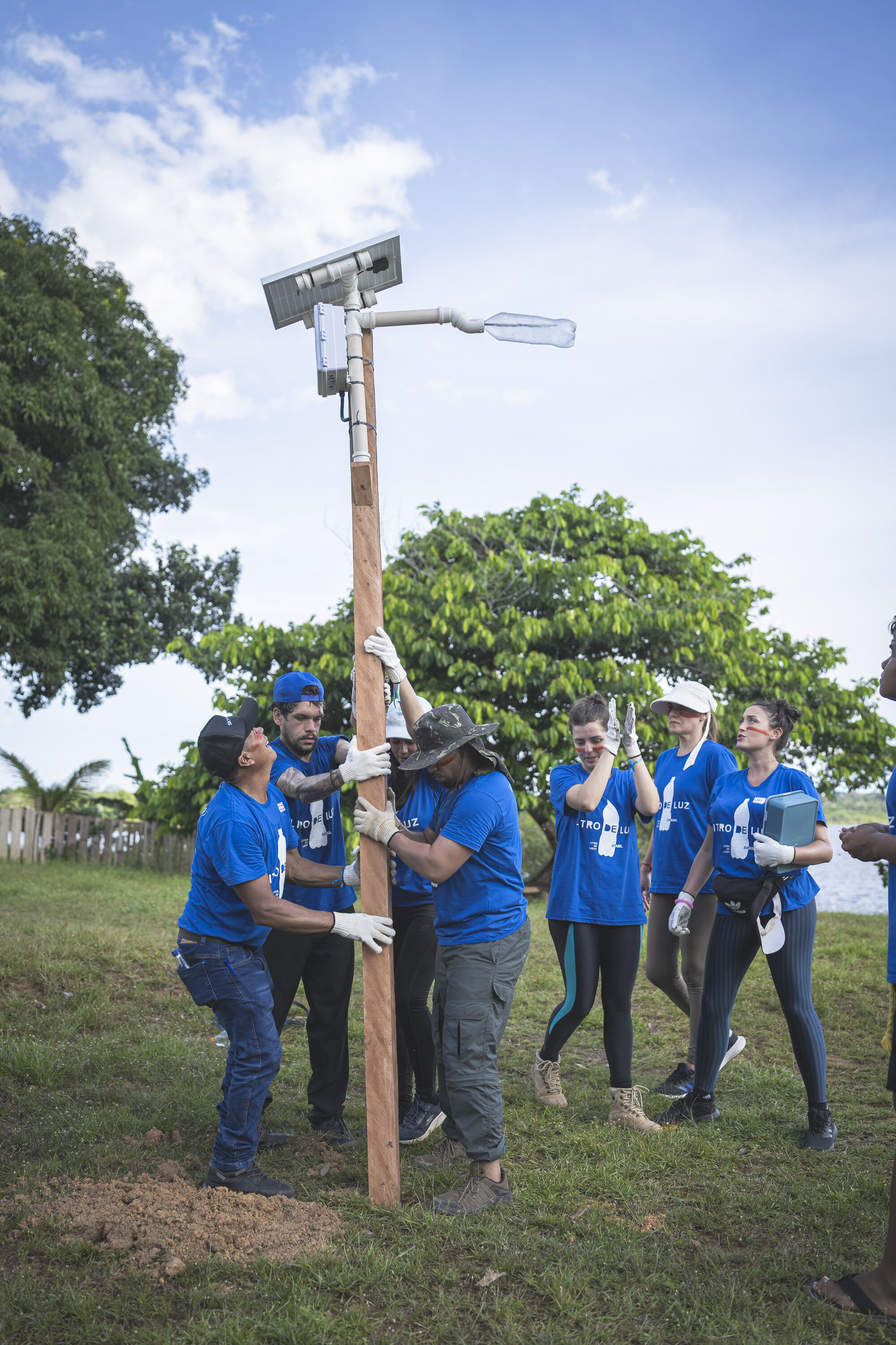 Solar lamps for Amazon communities without electricity: Audi and Litro de Luz continue partnership - Eight volunteers secure a wooden pole in the ground in a field in Brazil, to which a solar-powered street lamp is attached.