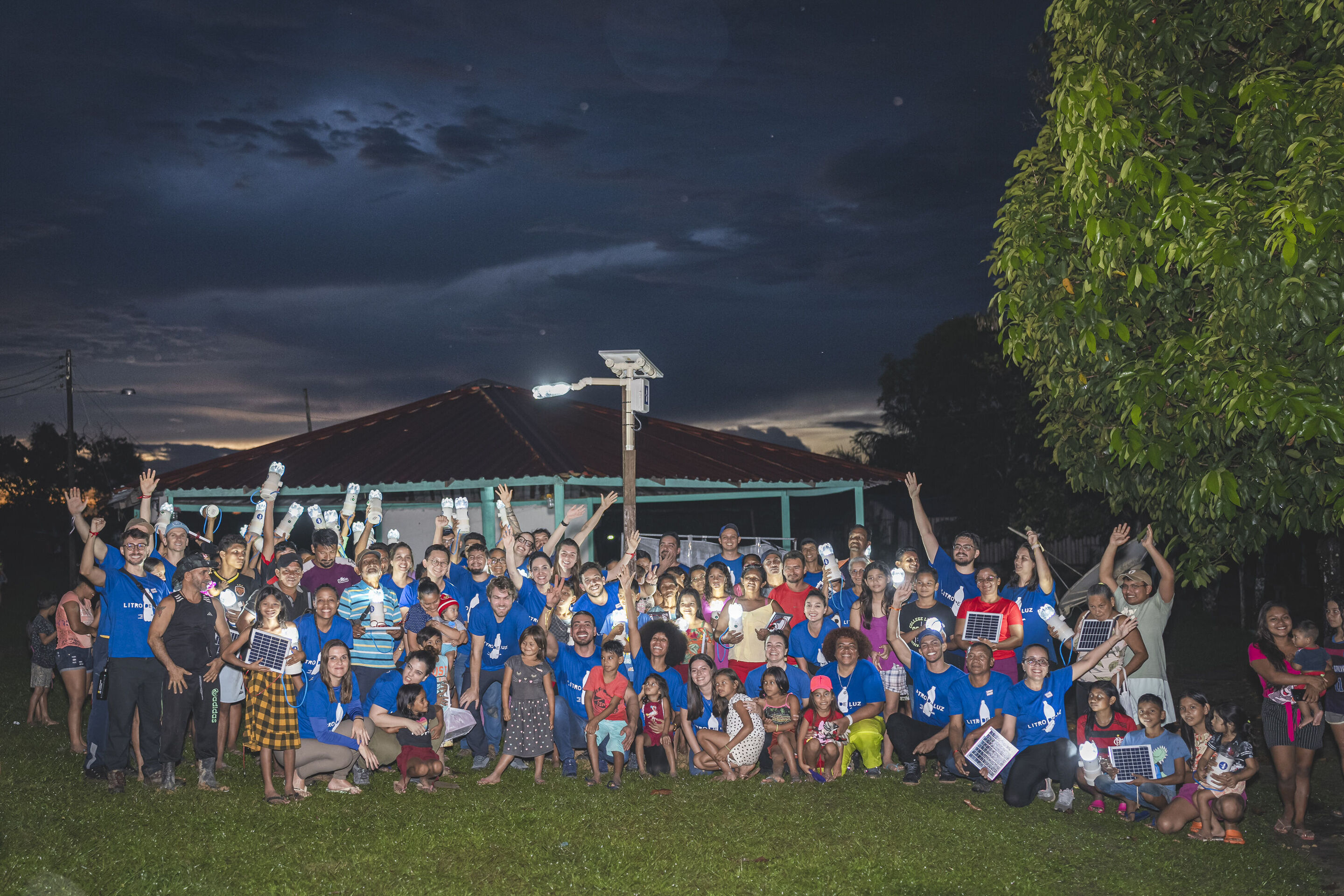 Solar lamps for Amazon communities without electricity: Audi and Litro de Luz continue partnership - A group photo of the volunteers and local residents in a field in Brazil in the dark. The people are posing for the picture under an illuminated solar-powered...