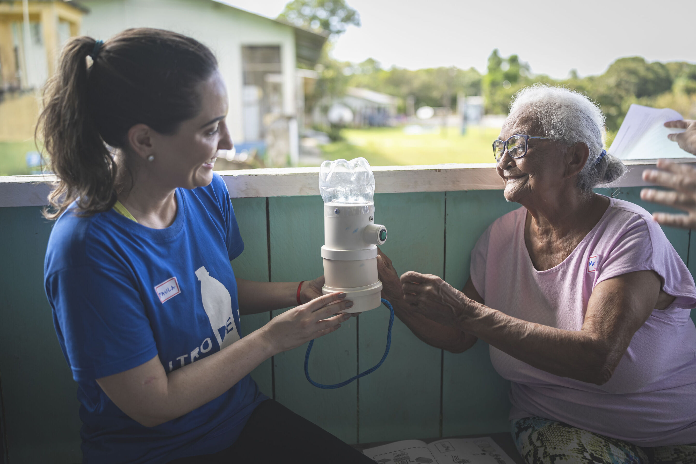 Solar lamps for Amazon communities without electricity: Audi and Litro de Luz continue partnership - Paula Barreiros, Head of Compliance, Quality & ESG at Audi do Brasil, sits on a veranda with a local resident and shows her a solar-powered lamp.