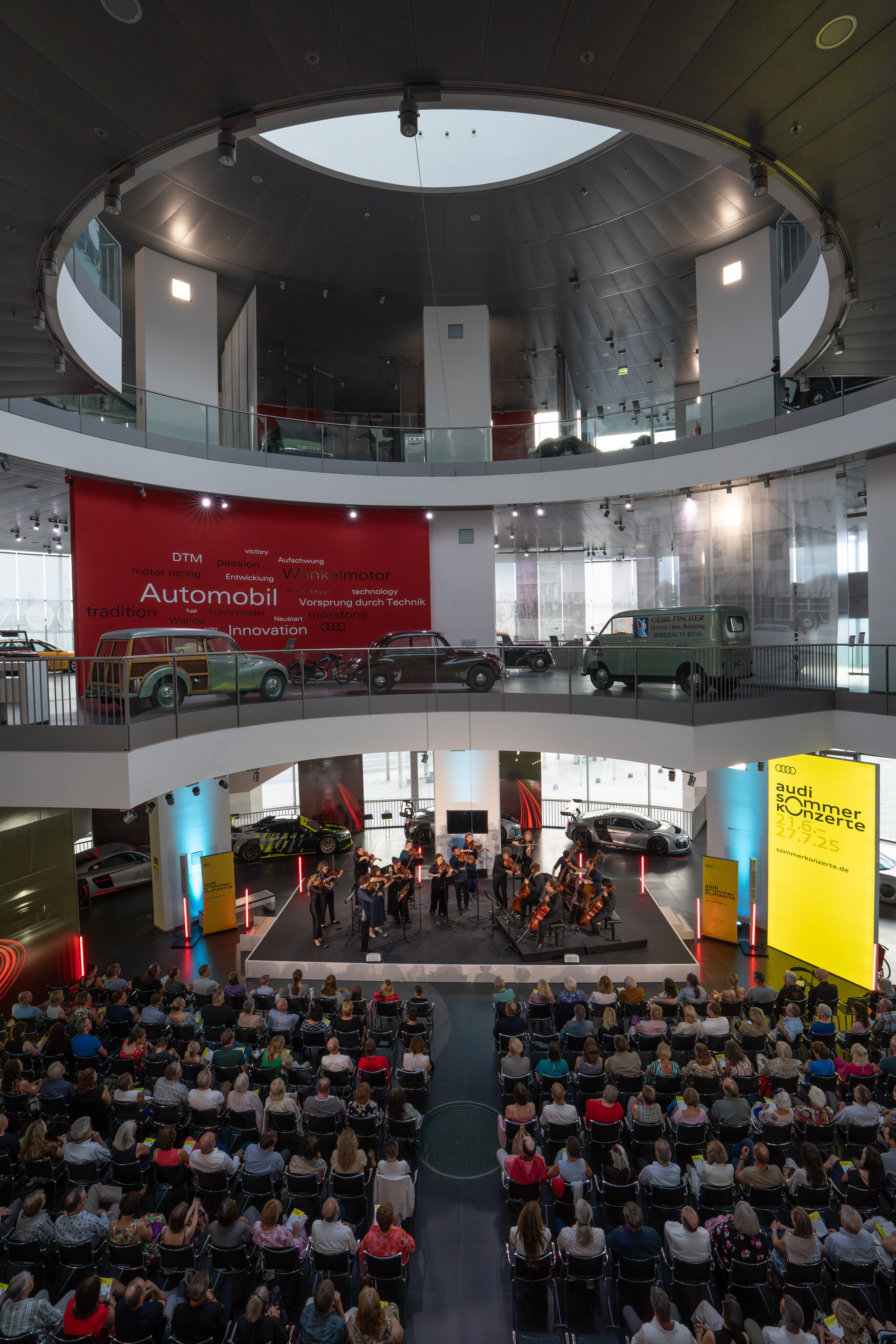 “Crossing over the Atlantic”: from Britten to Nirvana with the O/Modernt chamber orchestra - On the first level of the Audi museum mobile, the O/Modernt Chamber Orchestra, conducted by Hugo Ticciati, faces the audience. Above, two levels of the permanent...