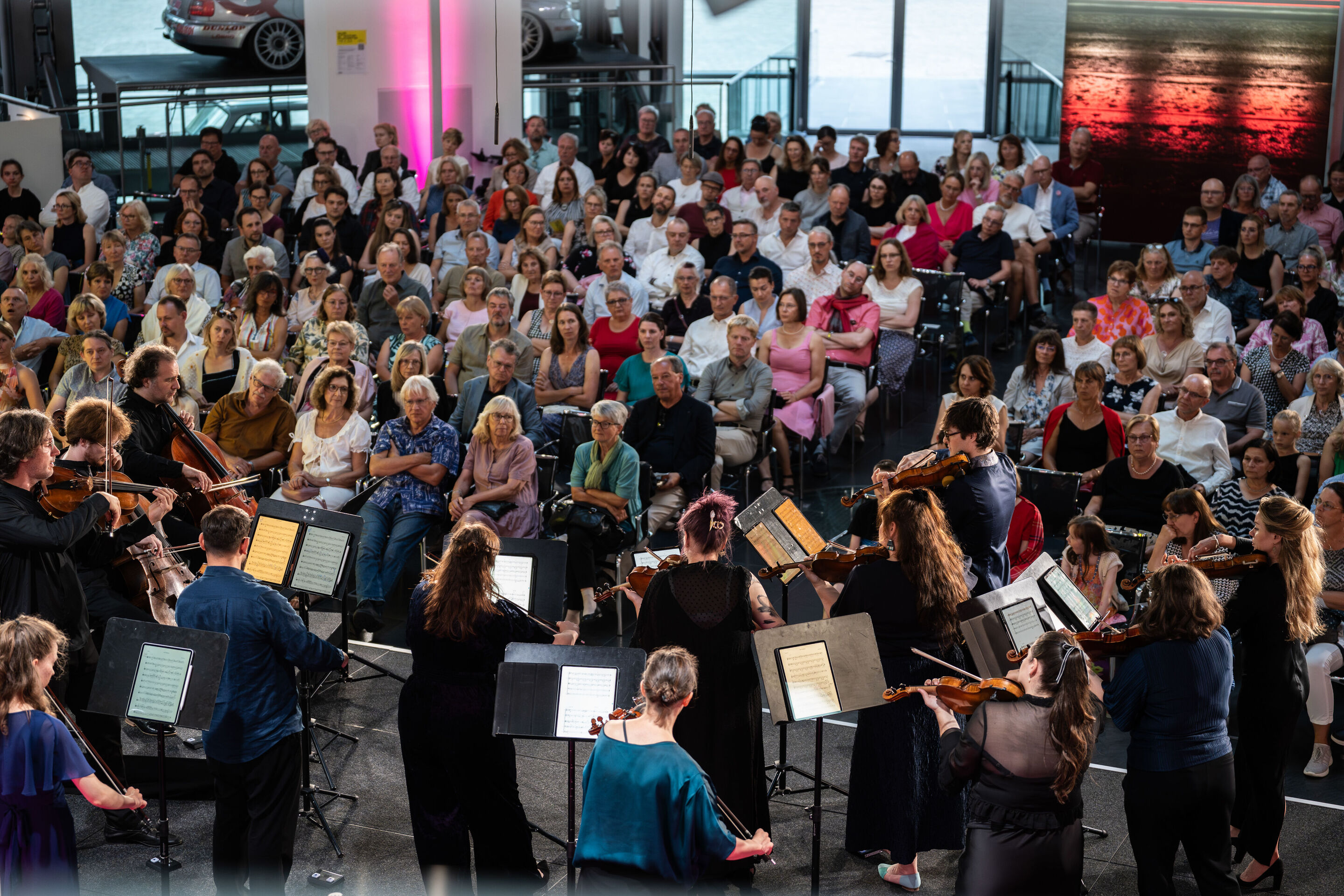 “Crossing over the Atlantic”: from Britten to Nirvana with the O/Modernt chamber orchestra - Seen from behind, part of the musicians of the O/Modernt Chamber Orchestra are on stage at the Audi museum mobile, facing the audience.