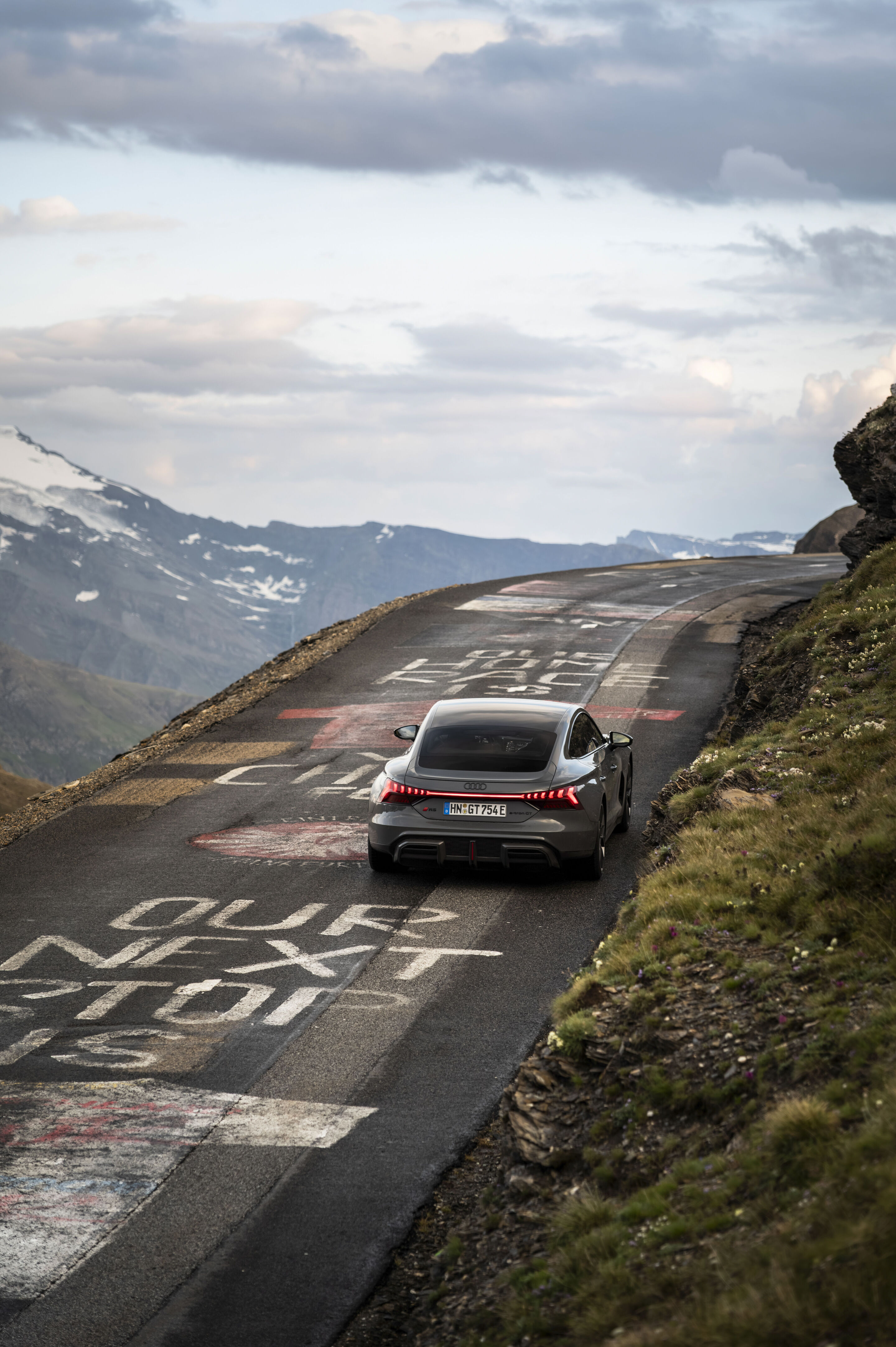 Audi RS e-tron GT quattro - Audi RS e-tron GT quattro in Nimbusgrau Perleffekt auf einer Bergstraße, umgeben von alpiner Landschaft und weitem Panoramablick.