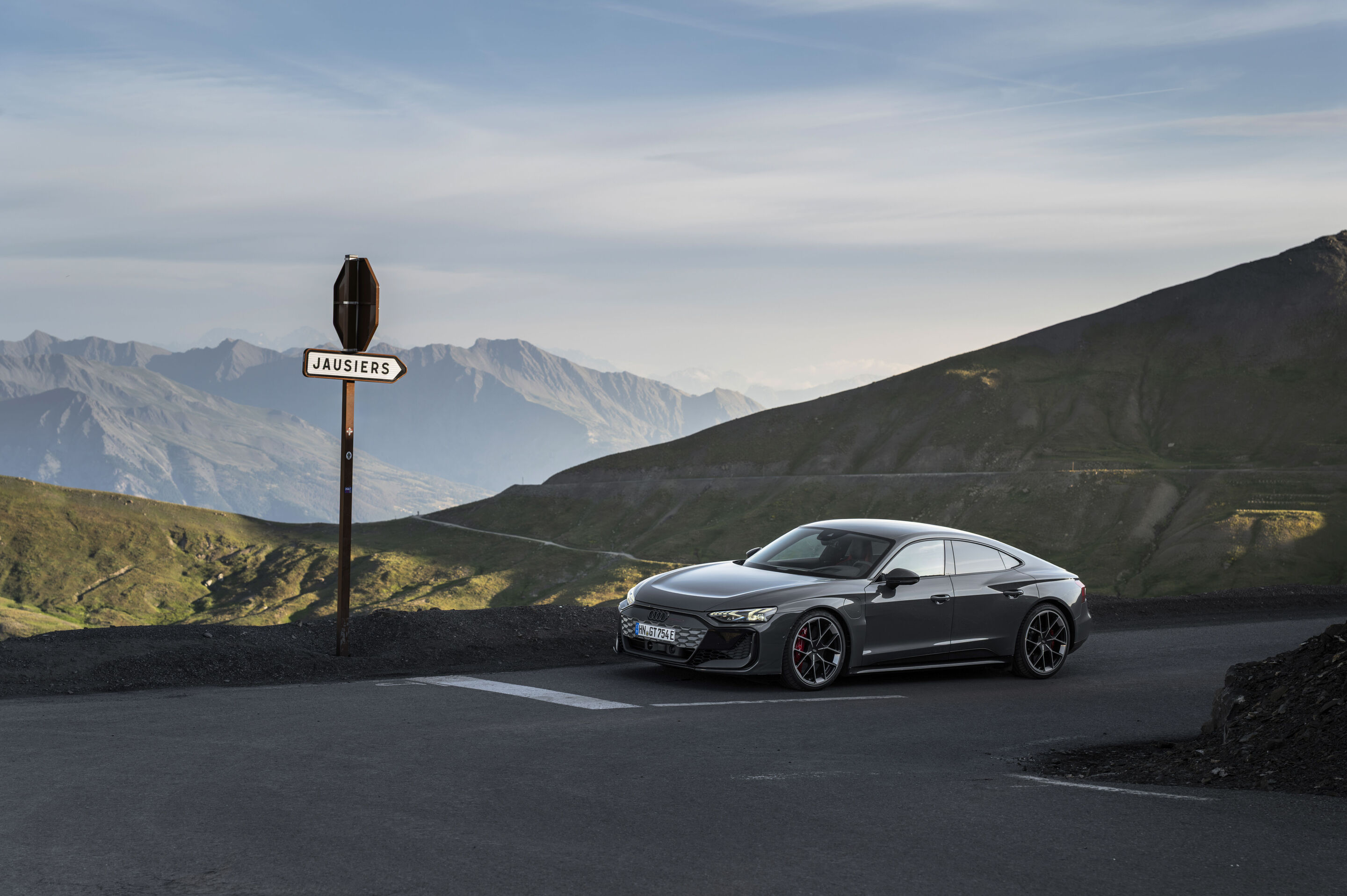 Audi RS e-tron GT quattro - Audi RS e-tron GT quattro in Nimbus Grey Pearl Effect on a mountain road with views of the surrounding peaks.