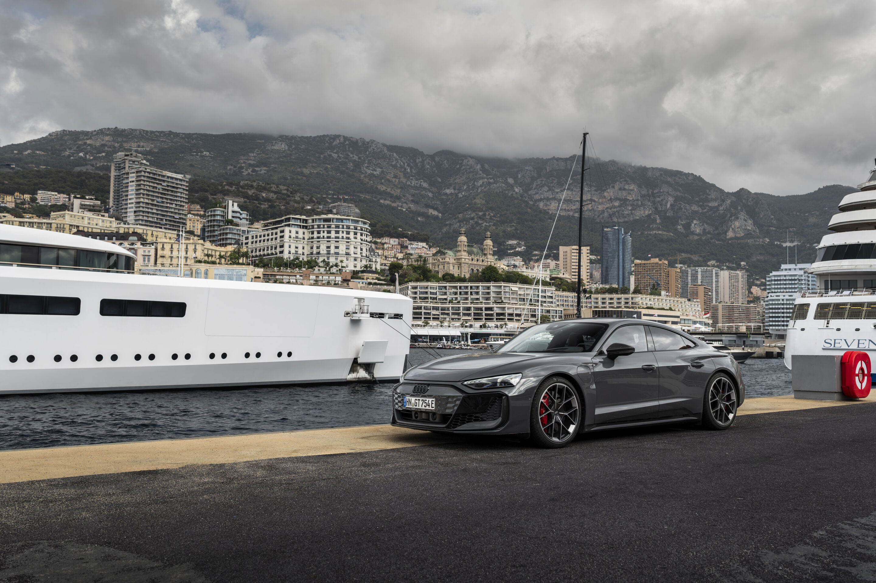 Audi RS e-tron GT quattro - Audi RS e-tron GT quattro in Nimbus Grey Pearl Effect at the harbor with yachts and a mountain landscape in the background.