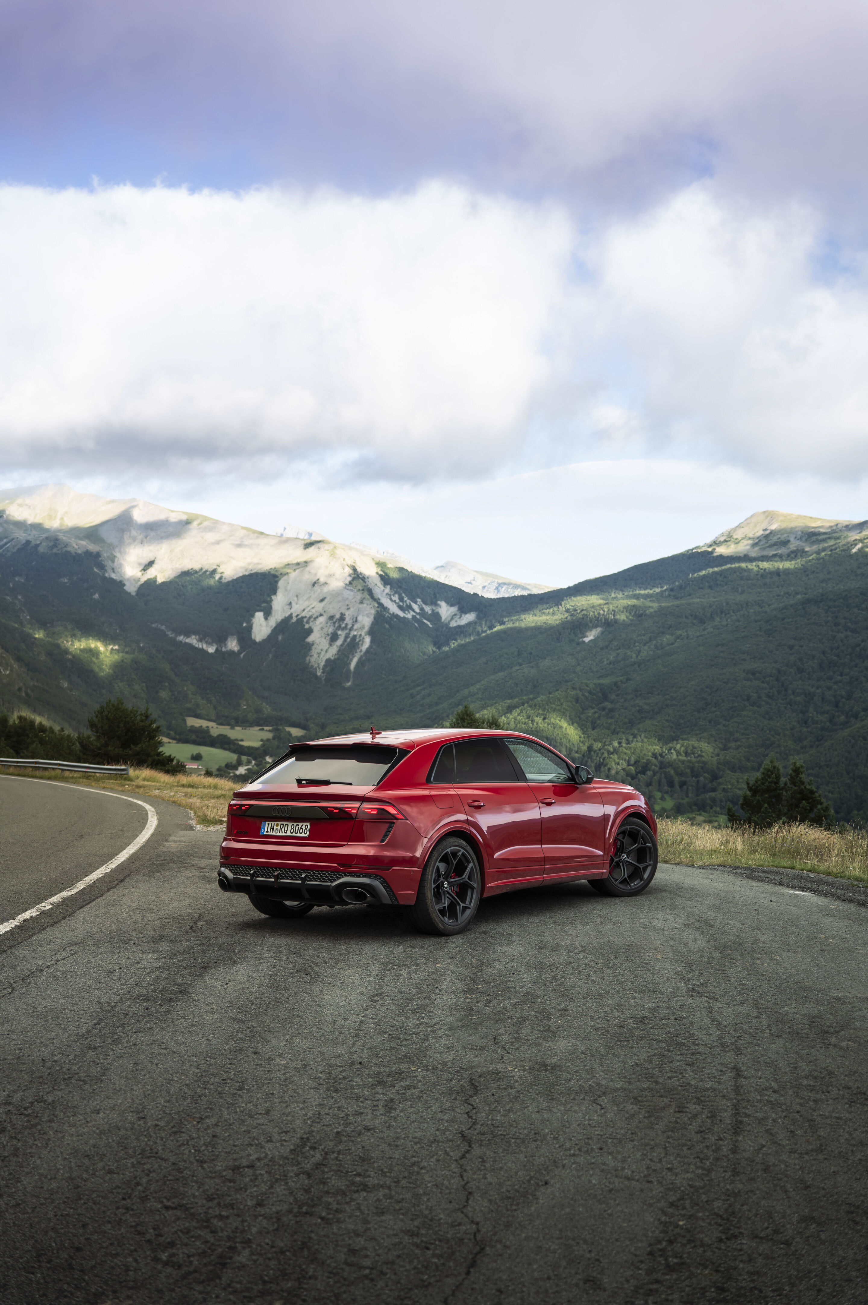 Audi RS Q8 SUV performance - Audi RS Q8 SUV performance in Chili Red Metallic on a winding mountain road against the backdrop of distinctive peaks.