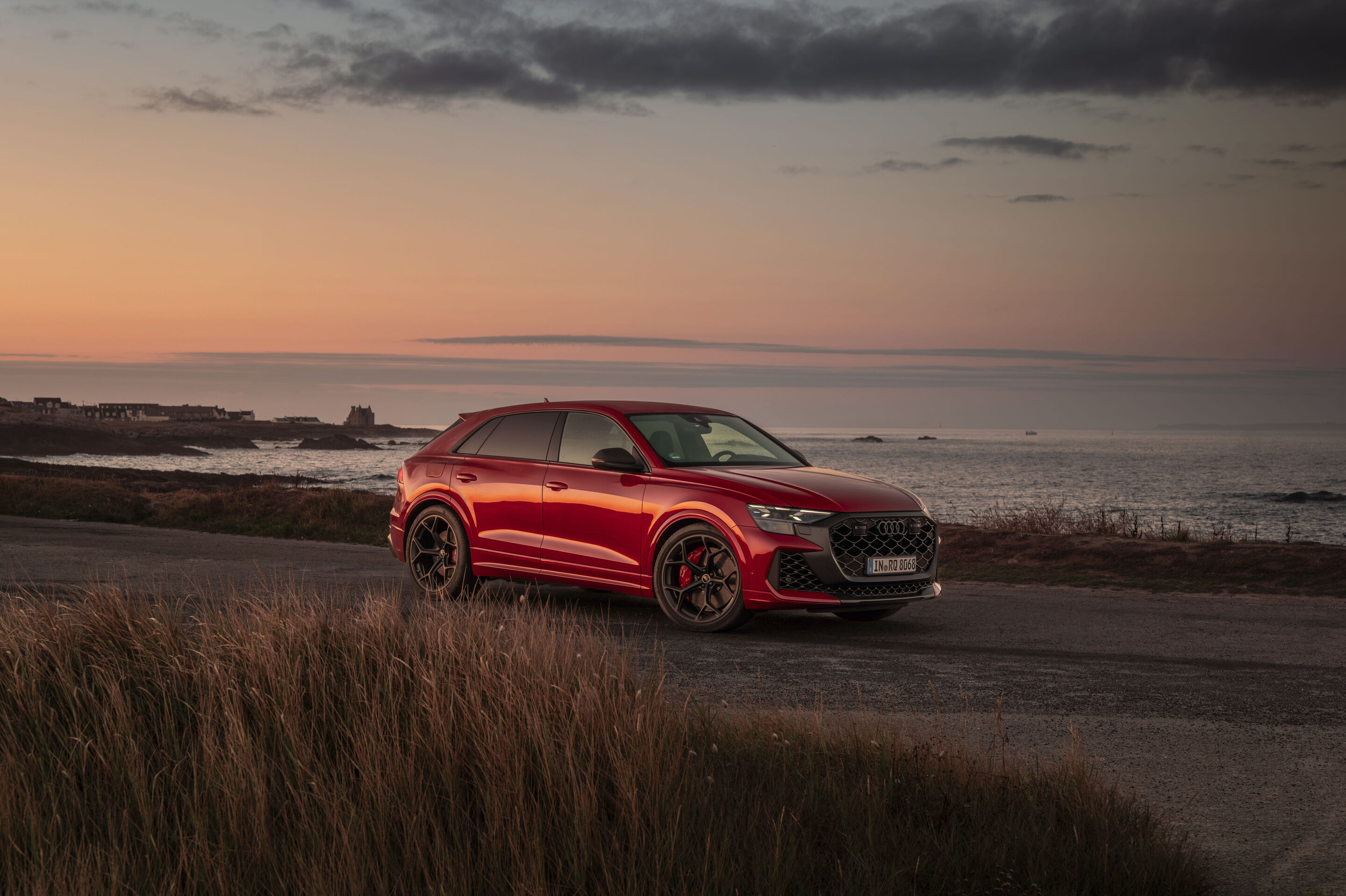Audi RS Q8 SUV performance - Audi RS Q8 SUV performance in Chili Red Metallic on a coastal road with the sunset over the sea in the background.