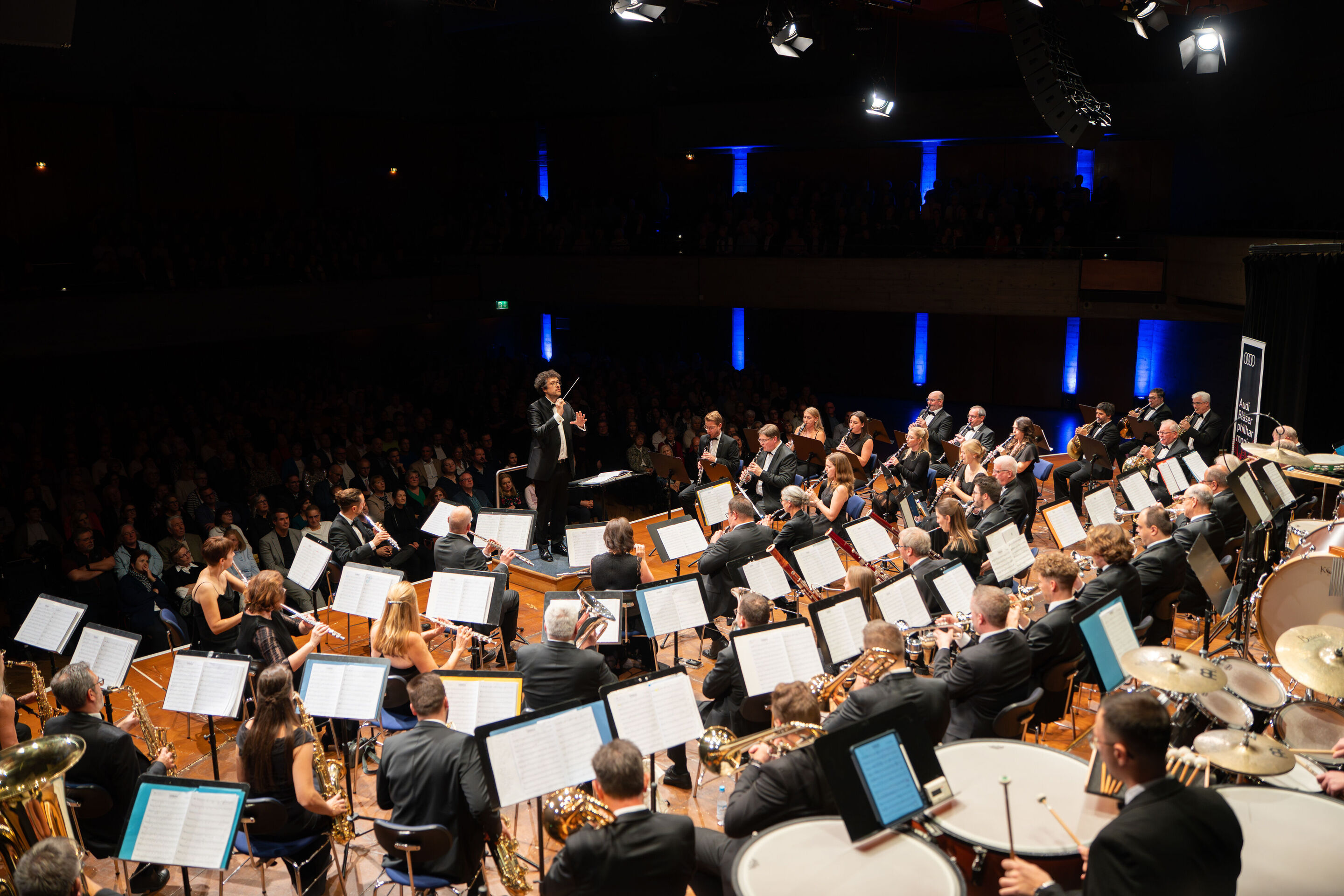 Benefizkonzert der Audi Bläserphilharmonie mit der Vienna Clarinet Connection - Blick von der Bühne Richtung Publikum: Pietro Sarno dirigiert beim Benefizkonzert 2025 die Audi Bläserphilharmonie, deren Mitglieder auf der Bühne im Festsaal Ingolstadt vor...