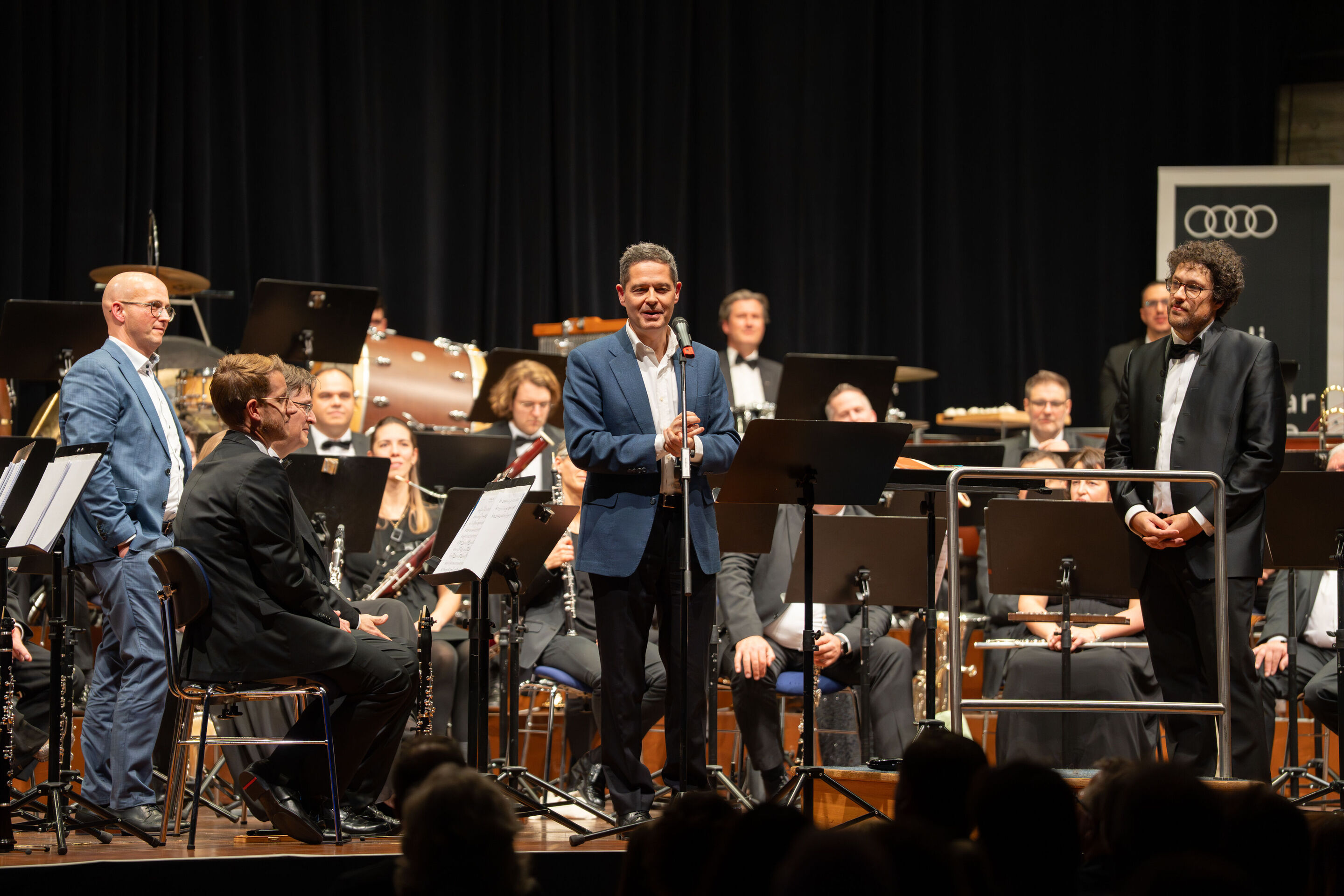 Benefizkonzert der Audi Bläserphilharmonie mit der Vienna Clarinet Connection - Xavier Ros, Audi Personalvorstand und Arbeitsdirektor, spricht beim Benefizkonzert der Audi Bläserphilharmonie 2025 auf der Bühne im Festsaal Ingolstadt zum Publikum; links...