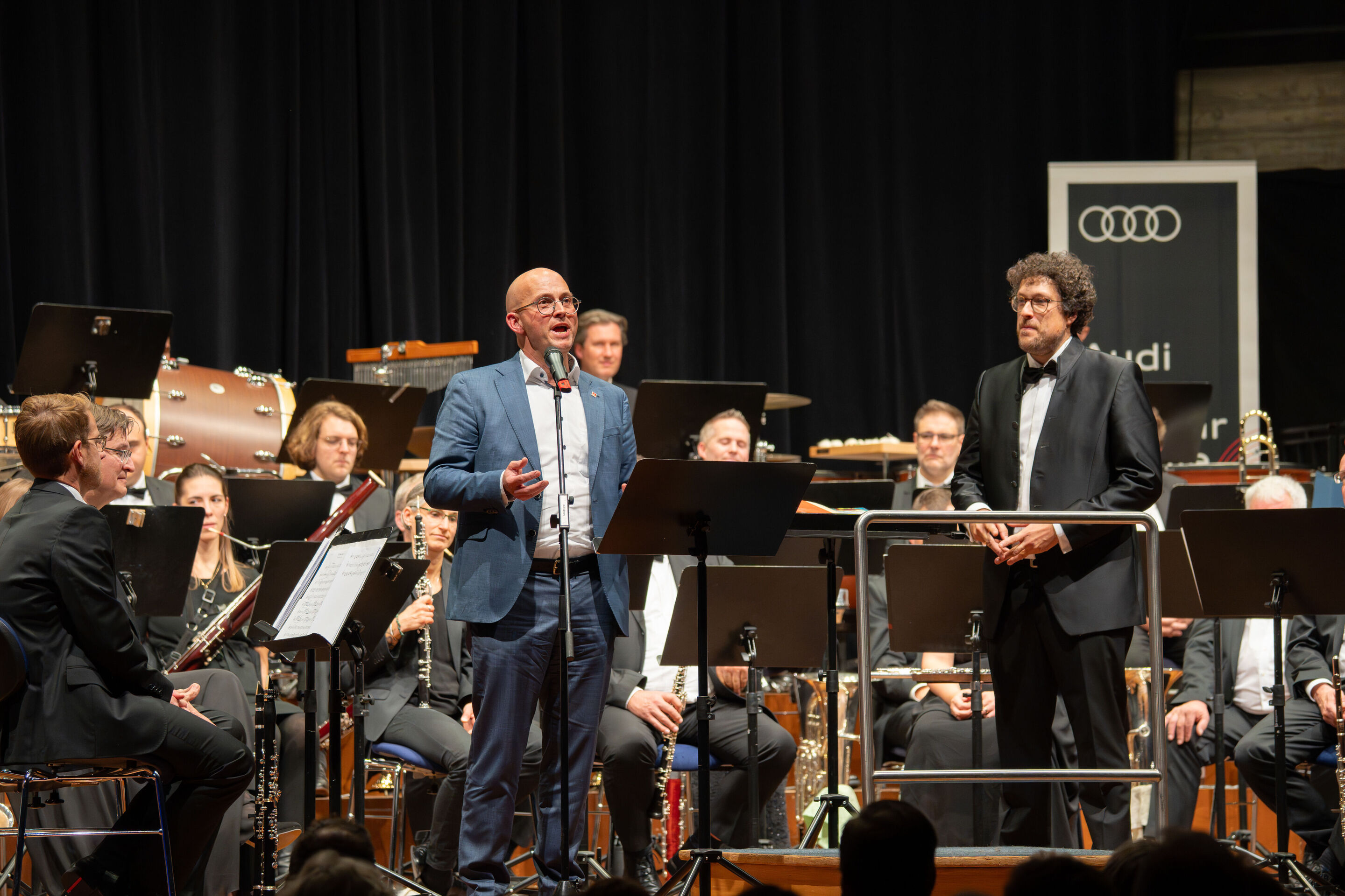 Benefizkonzert der Audi Bläserphilharmonie mit der Vienna Clarinet Connection - Jörg Schlagbauer, Audi Betriebsratsvorsitzender, spricht beim Benefizkonzert der Audi Bläserphilharmonie 2025 auf der Bühne im Festsaal Ingolstadt zum Publikum; rechts im...