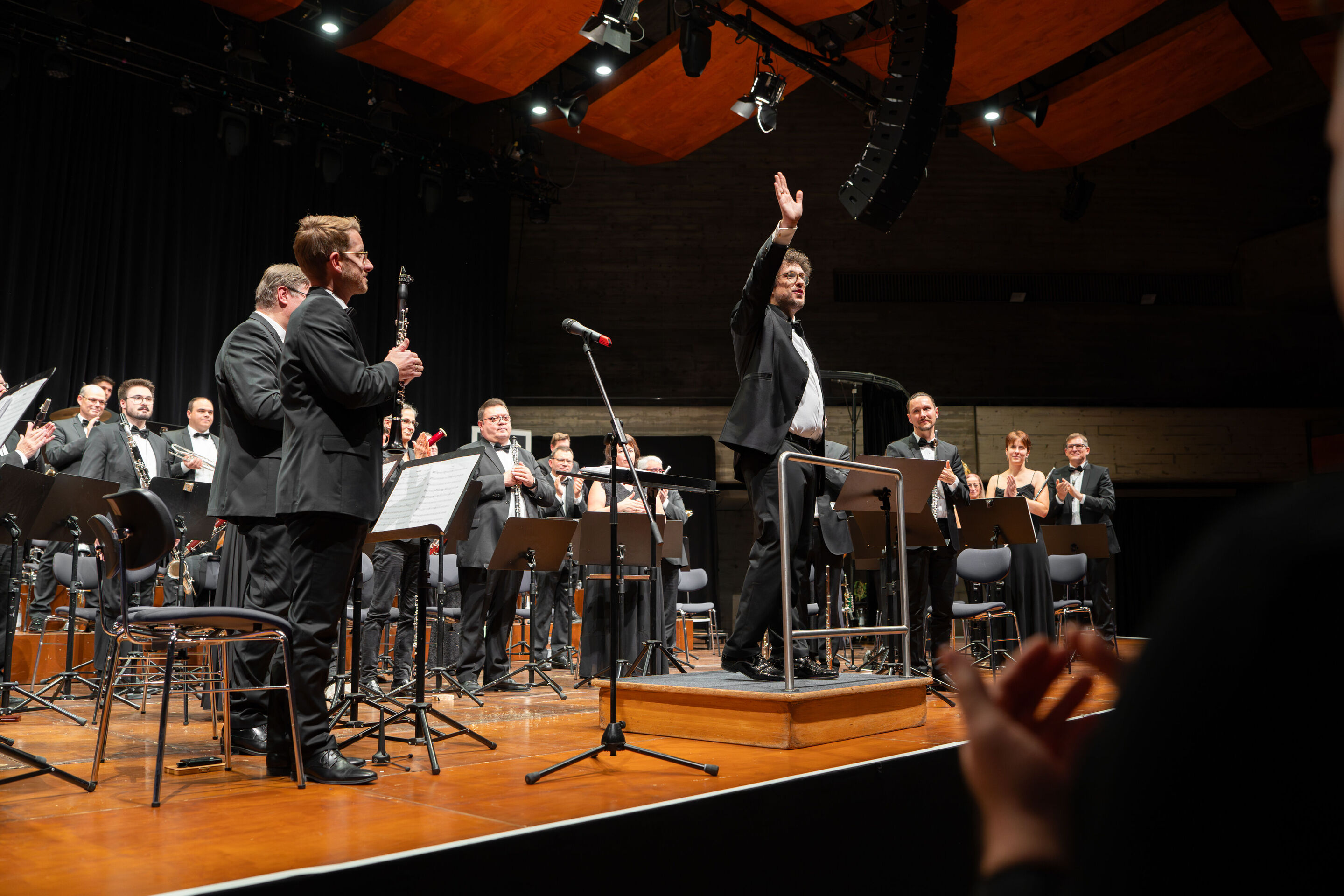 Benefizkonzert der Audi Bläserphilharmonie mit der Vienna Clarinet Connection - Pietro Sarno, künstlerischer Leiter der Audi Bläserphilharmonie, steht beim Benefizkonzert 2025 auf dem Dirigentenpodium und winkt in Richtung des Publikums; hinter ihm steht...