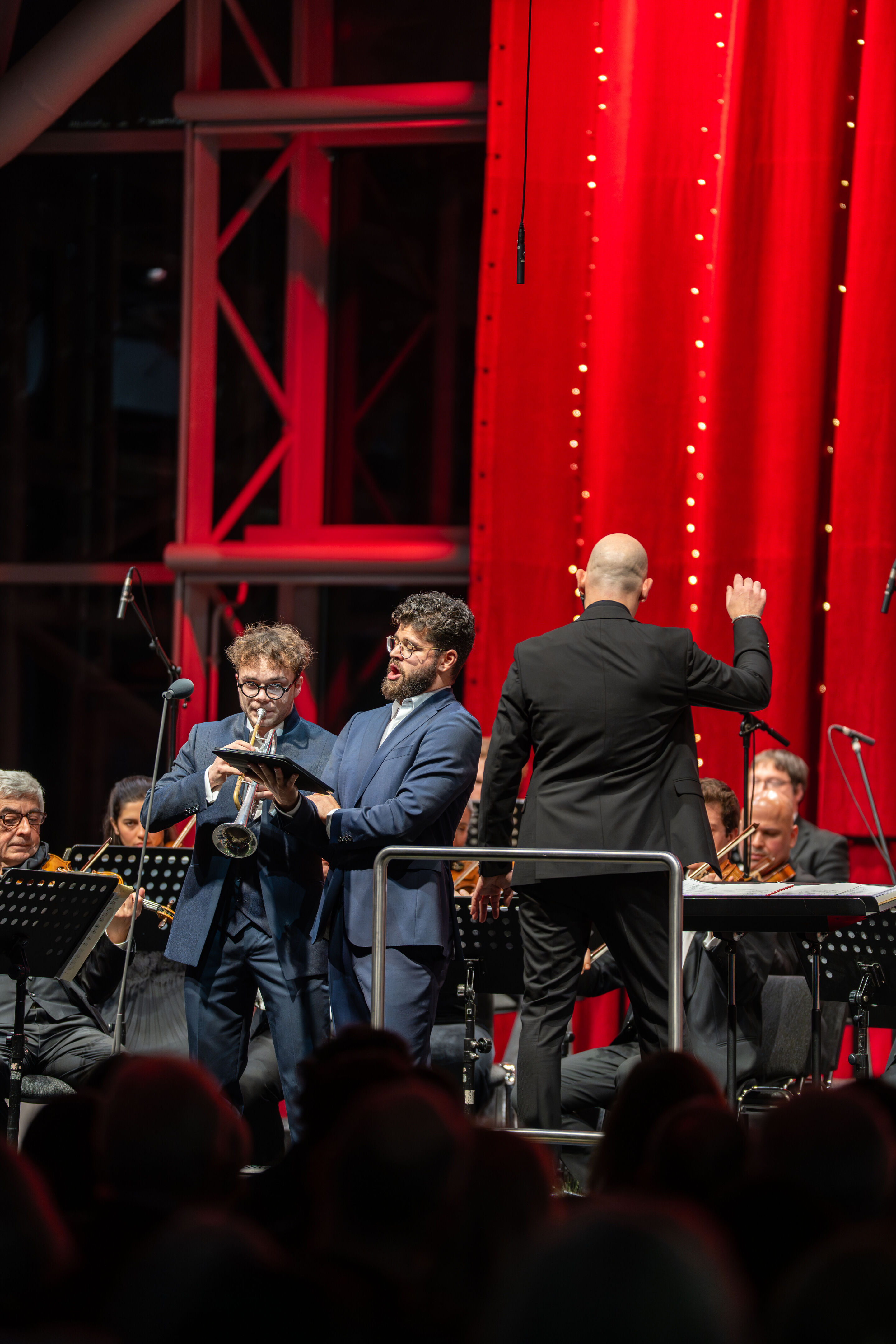 Audi Weihnachtskonzert 2025 - Trompeter Robin Paillet, Vokalist Lukas Enoch Lemcke (Bass) und Dirigent Ariel Zuckermann (v. l.) auf der Bühne beim Audi Weihnachtskonzert 2025