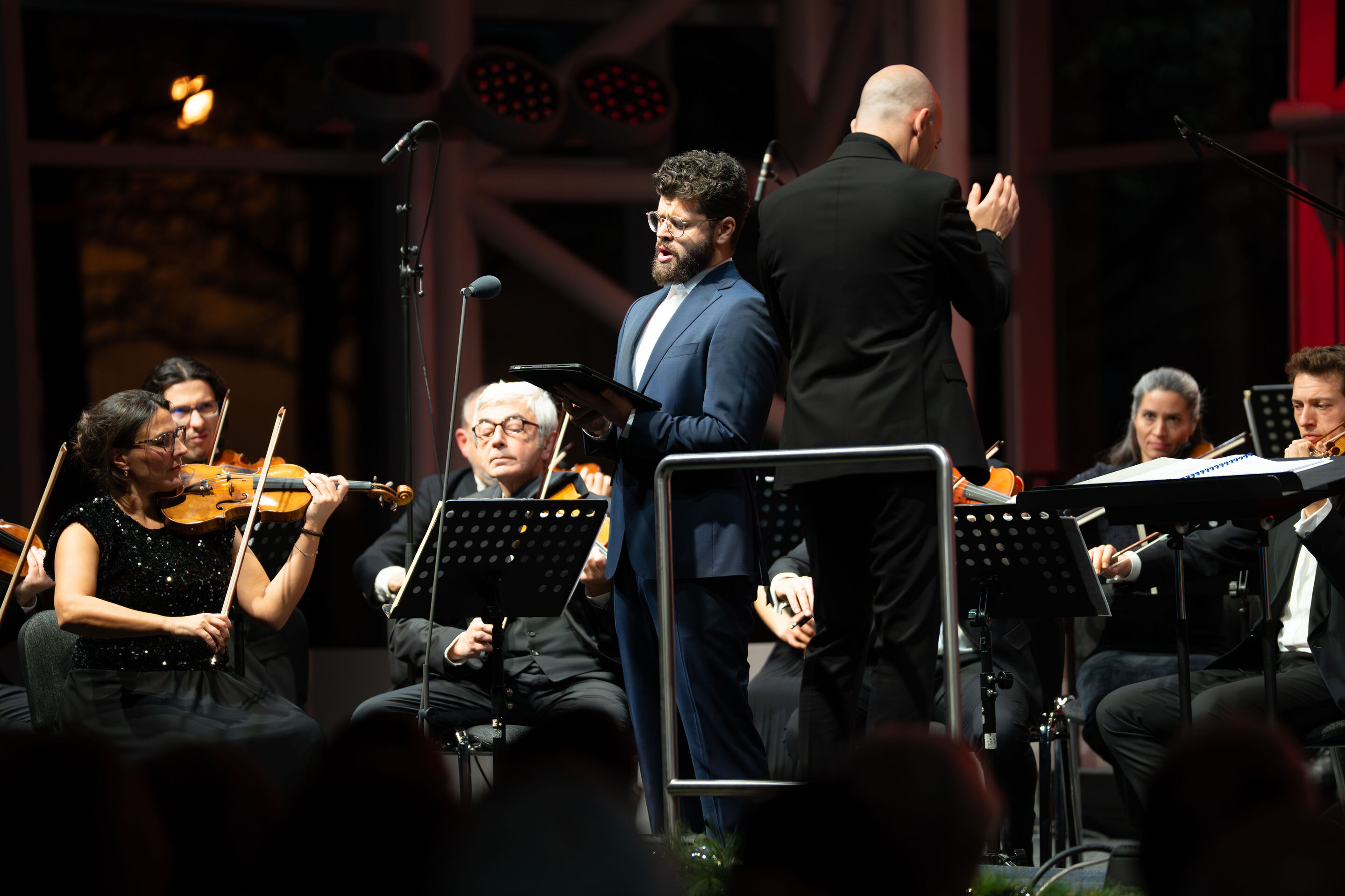 Audi Weihnachtskonzert 2025 - Vokalist Lukas Enoch Lemcke (Bass) und die Kammerphilharmonie Ingolstadt, unter der Leitung von Ariel Zuckermann, auf der Bühne beim Audi Weihnachtskonzert 2025