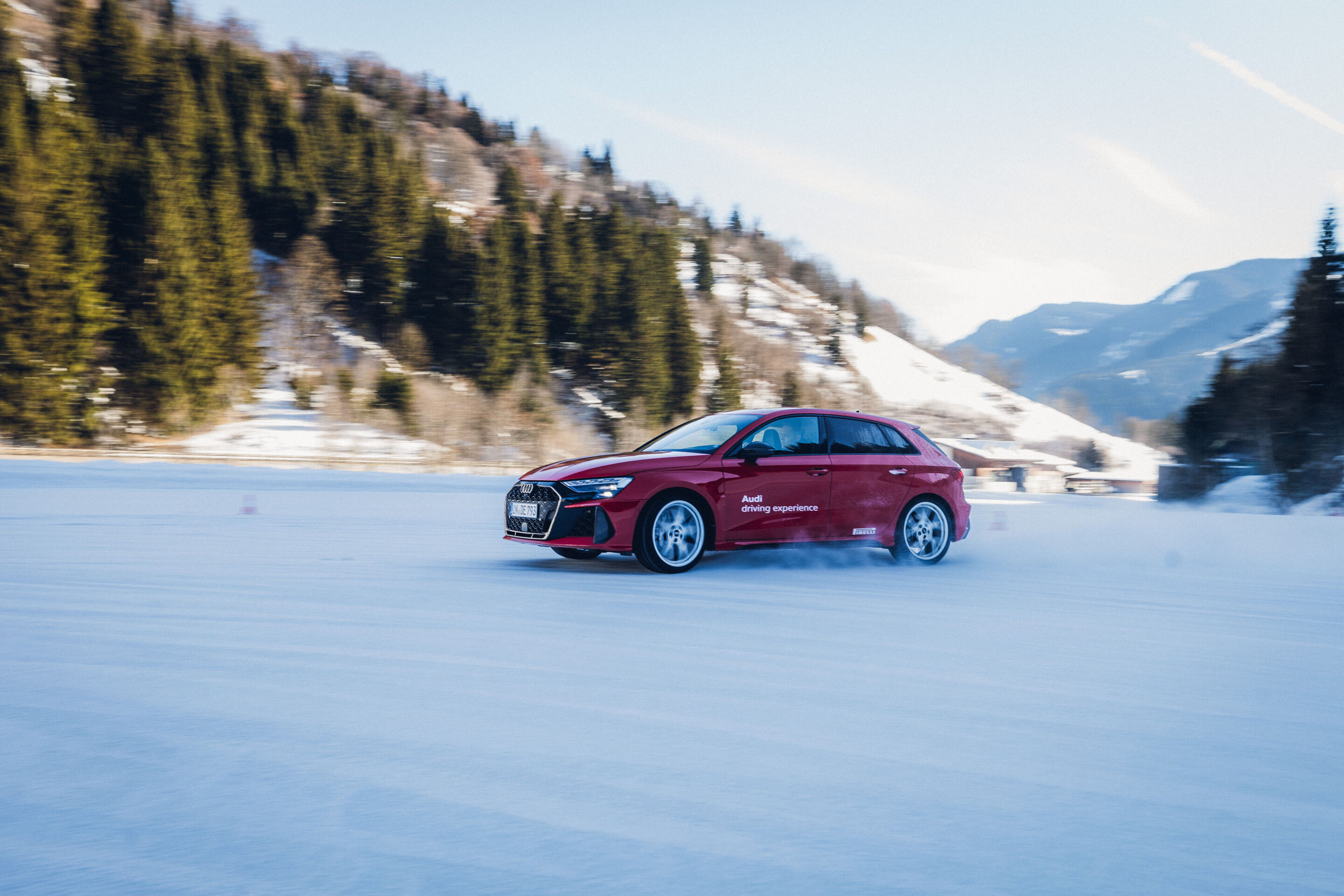 Audi RS 3 Sportback - An Audi RS 3 Sportback in Progressive Red is driving across a snowy surface, kicking up snow.