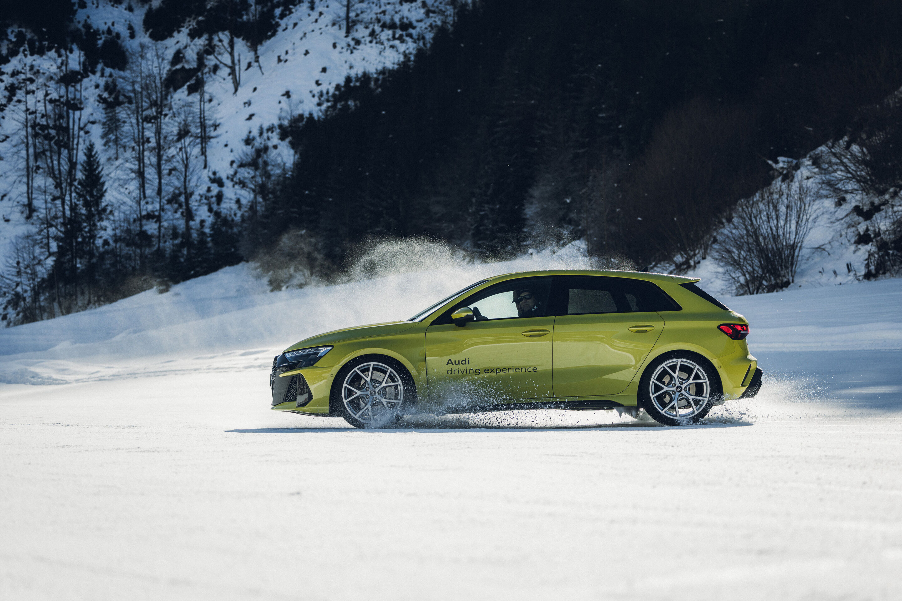 Audi RS 3 Sportback - An Audi RS 3 Sportback in Python Yellow is driving across a snowy surface, kicking up snow.