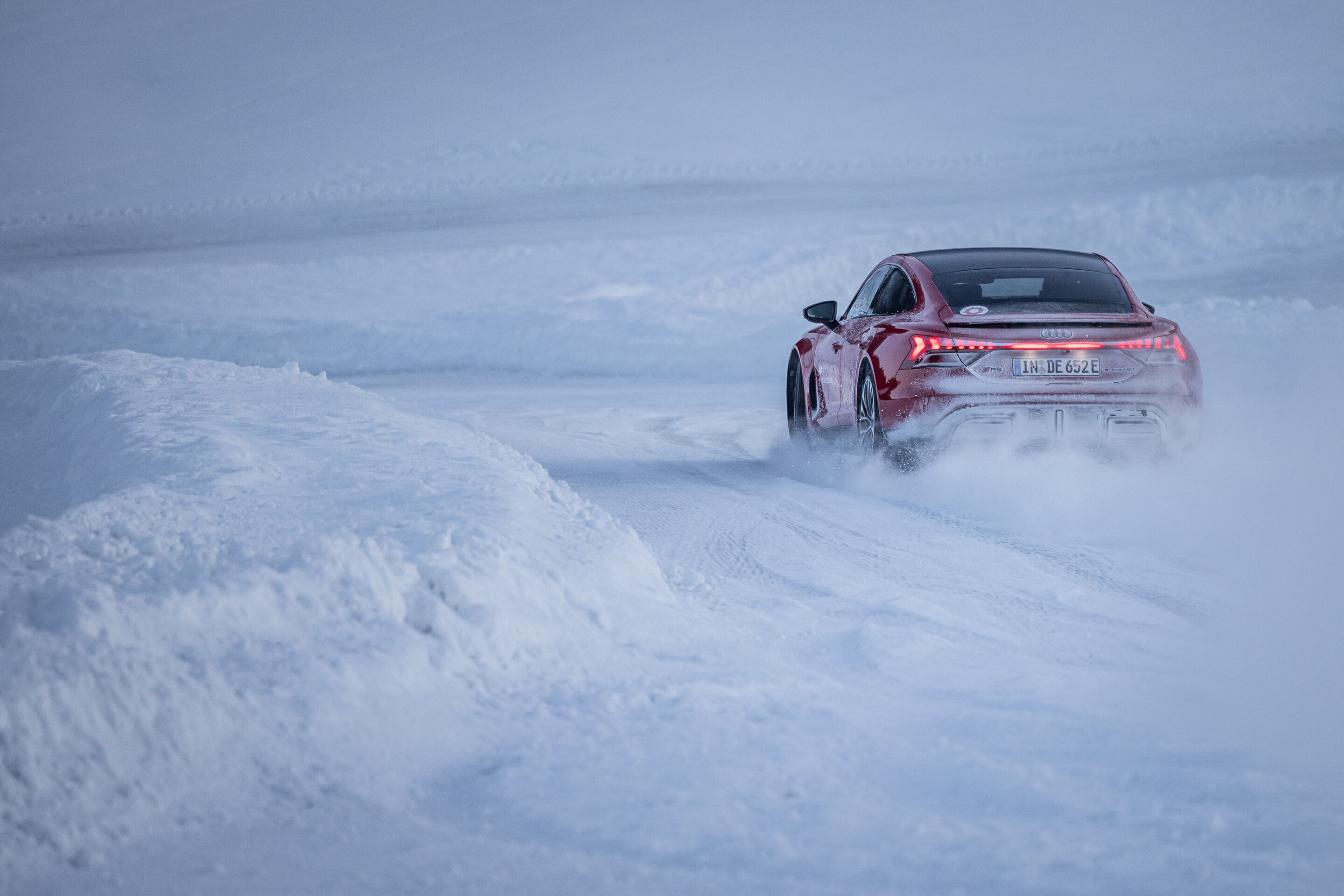 Audi RS e-tron GT - The Audi RS e-tron GT on a snow-covered test track, kicking up fine snow behind it.
Color: Progressive Red Metallic, outdoor dynamic shot, exterior, three-quarter rear view.