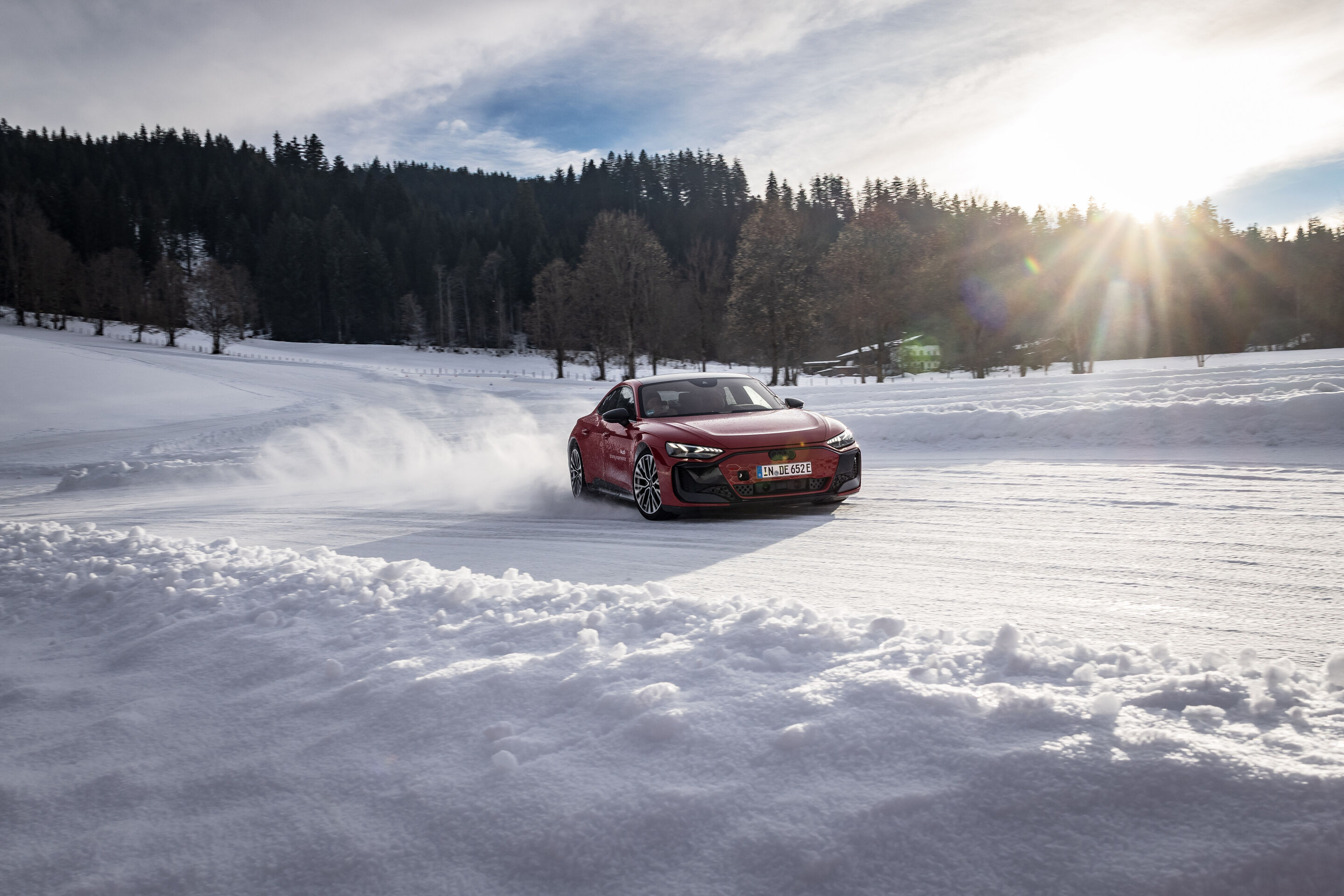 Audi RS e-tron GT - The Audi RS e-tron GT drives dynamically across a snow-covered track, kicking up snow as it moves, with a forest in the background under the low winter sun.
Color: Progressive Red Metallic, outdoor driving shot, exterior, three-quarter...