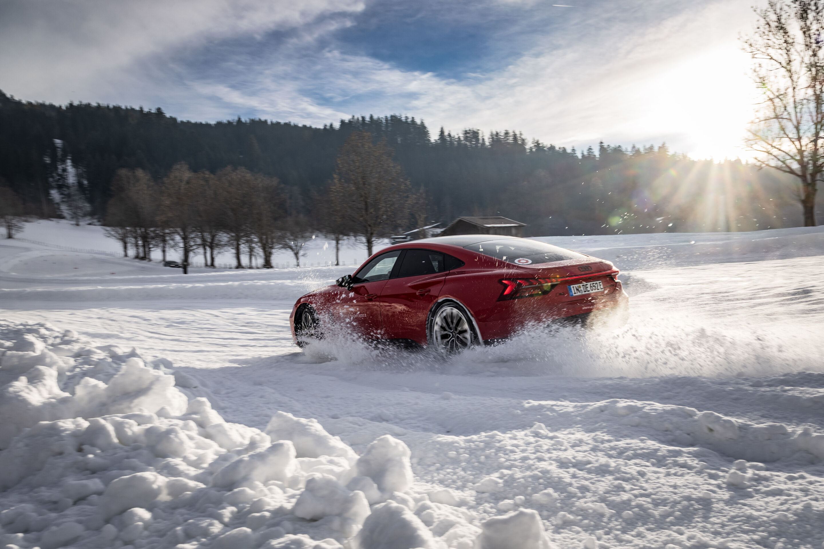 Audi RS e-tron GT - The Audi RS e-tron GT drives dynamically across a snow-covered track, kicking up snow as it moves, with a forest in the background under the low winter sun.
Color: Progressive Red Metallic, outdoor driving shot, exterior, three-quarter...
