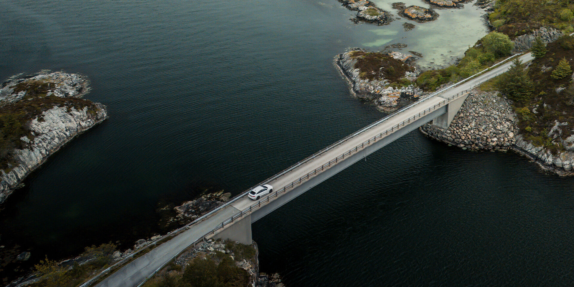 Audi A6 Sportback e-tron - An Audi A6 Sportback e-tron in Glacier white metallic drives over the Hardanger Bridge in Norway. Wooded mountains are visible in the background.