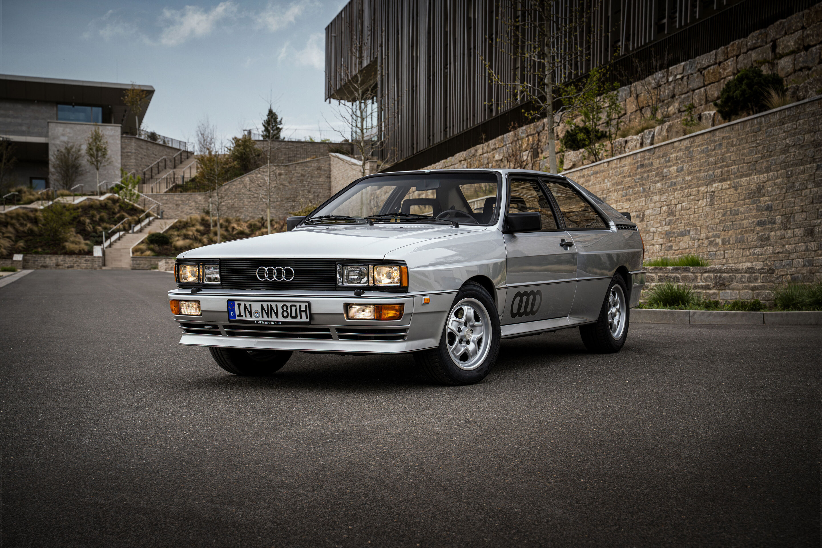 50 years of the Audi five-cylinder - A silver 1980 Audi quattro with flared wheel arches is presented in a three-quarter front view on an asphalt surface.