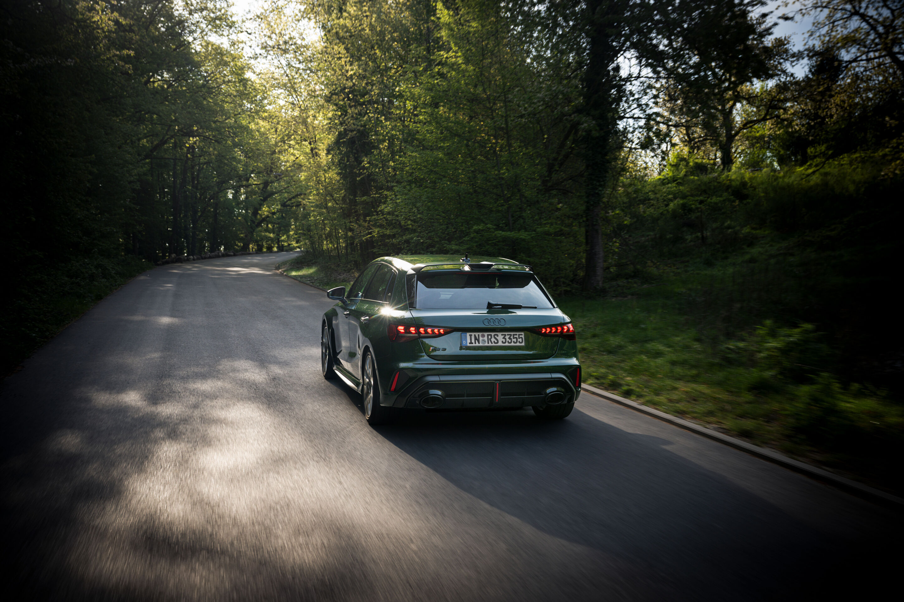 50 years of the Audi five-cylinder - An Audi RS3 competition limited (Malachite green) is driving along a forest road, captured from the rear with motion blur.