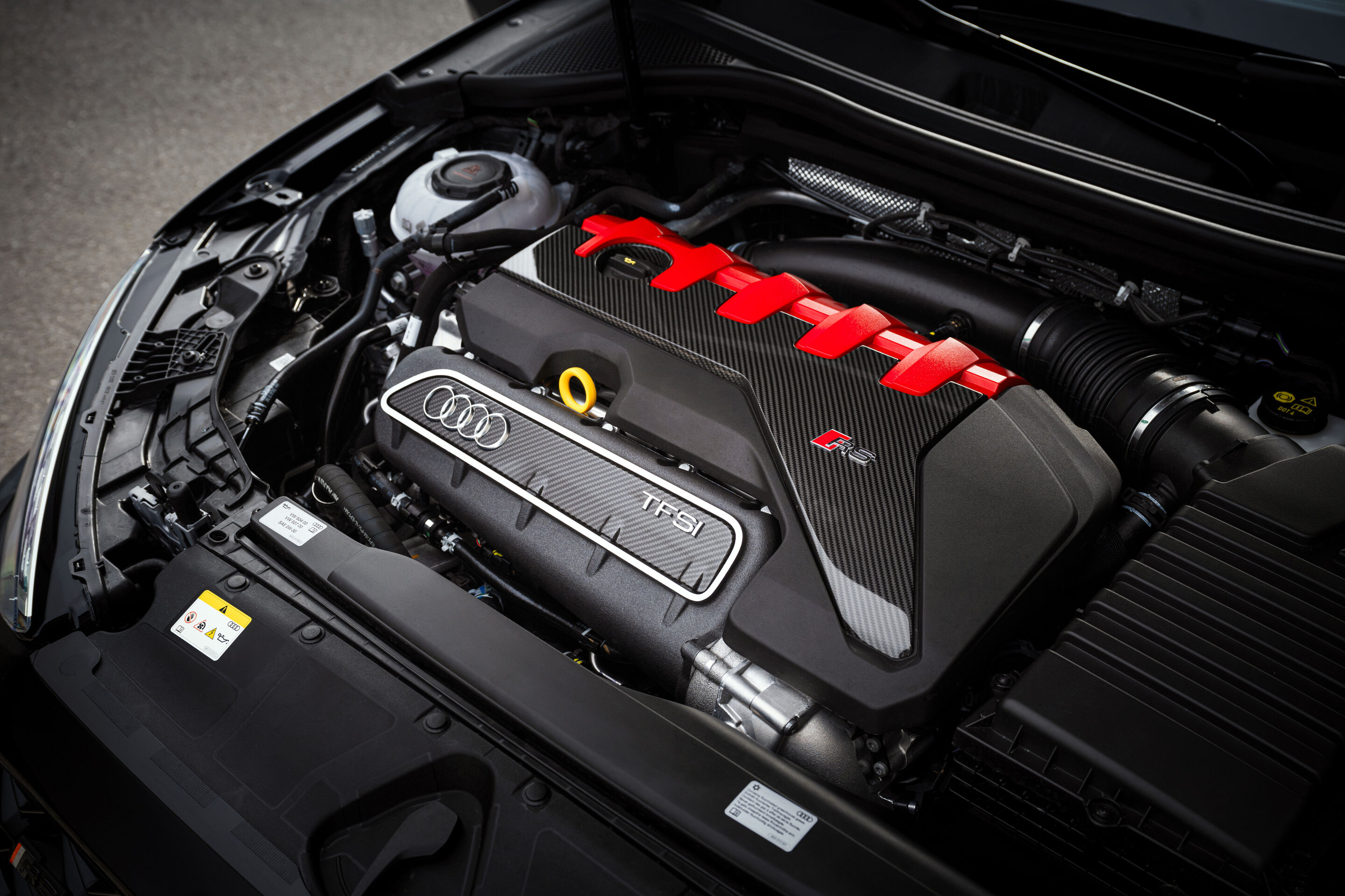 50 years of the Audi five-cylinder - The open engine bay of an Audi RS3 competition limited reveals the five-cylinder TFSI engine with a carbon-fiber cover and red accents.