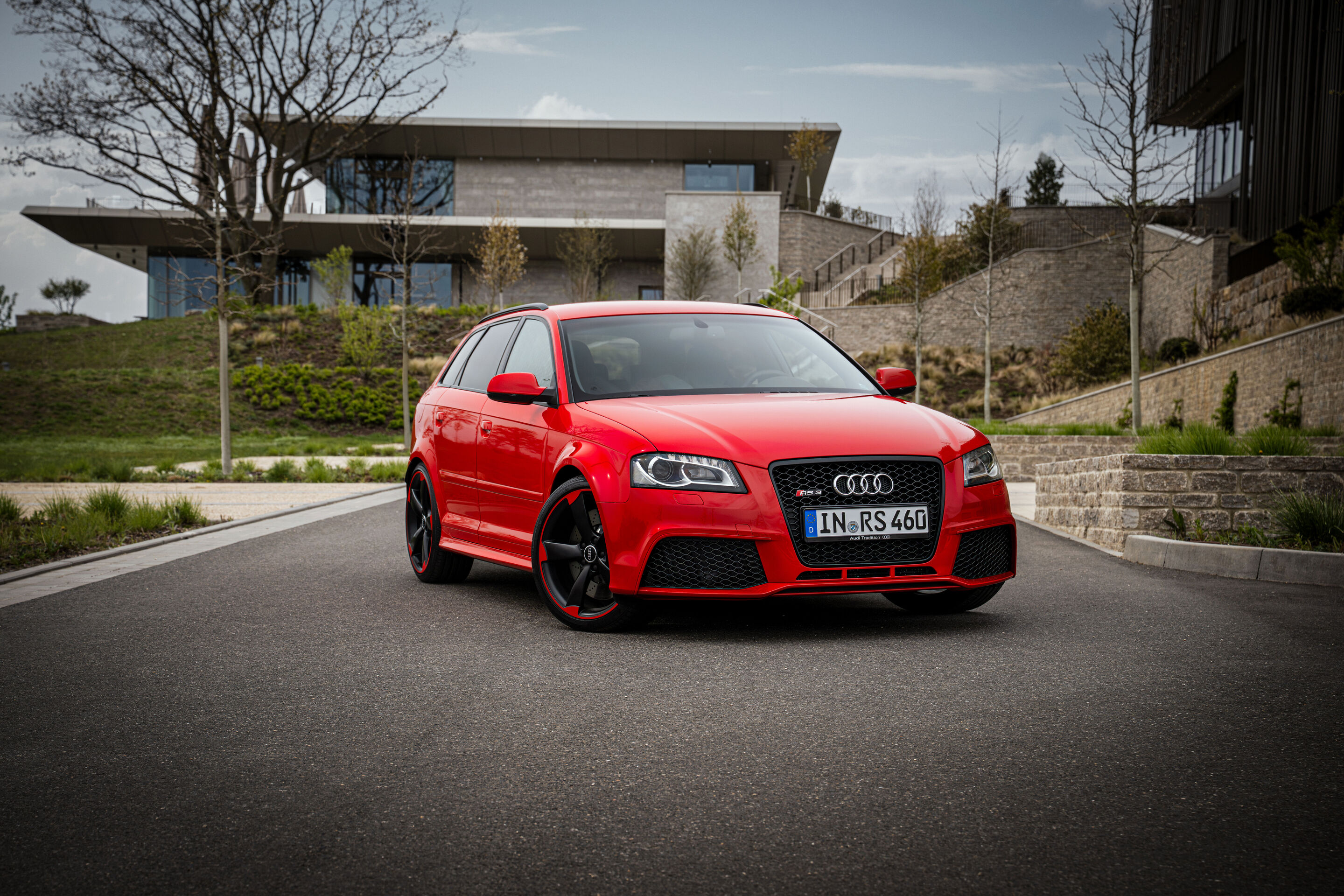 50 years of the Audi five-cylinder - A red 2011 Audi RS3 Sportback is parked on a paved roadway, shown in a three-quarter front view.
