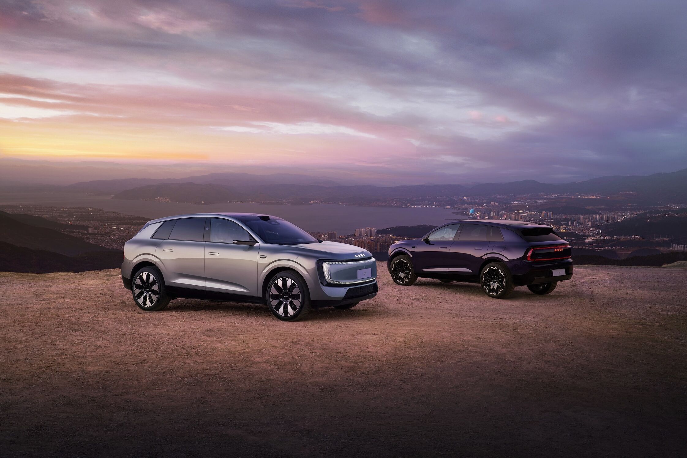 Audi at Auto China 2026 - Audi E7X, outdoor static shot, exterior, front three-quarter and rear three-quarter view against an urban landscape at dusk